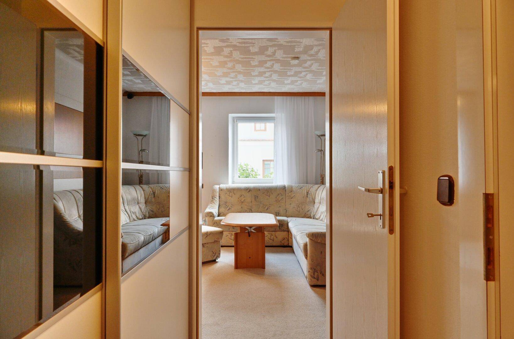 Flur mit Spiegelflächen und Blick in das helle Wohnzimmer mit Ecksofa.