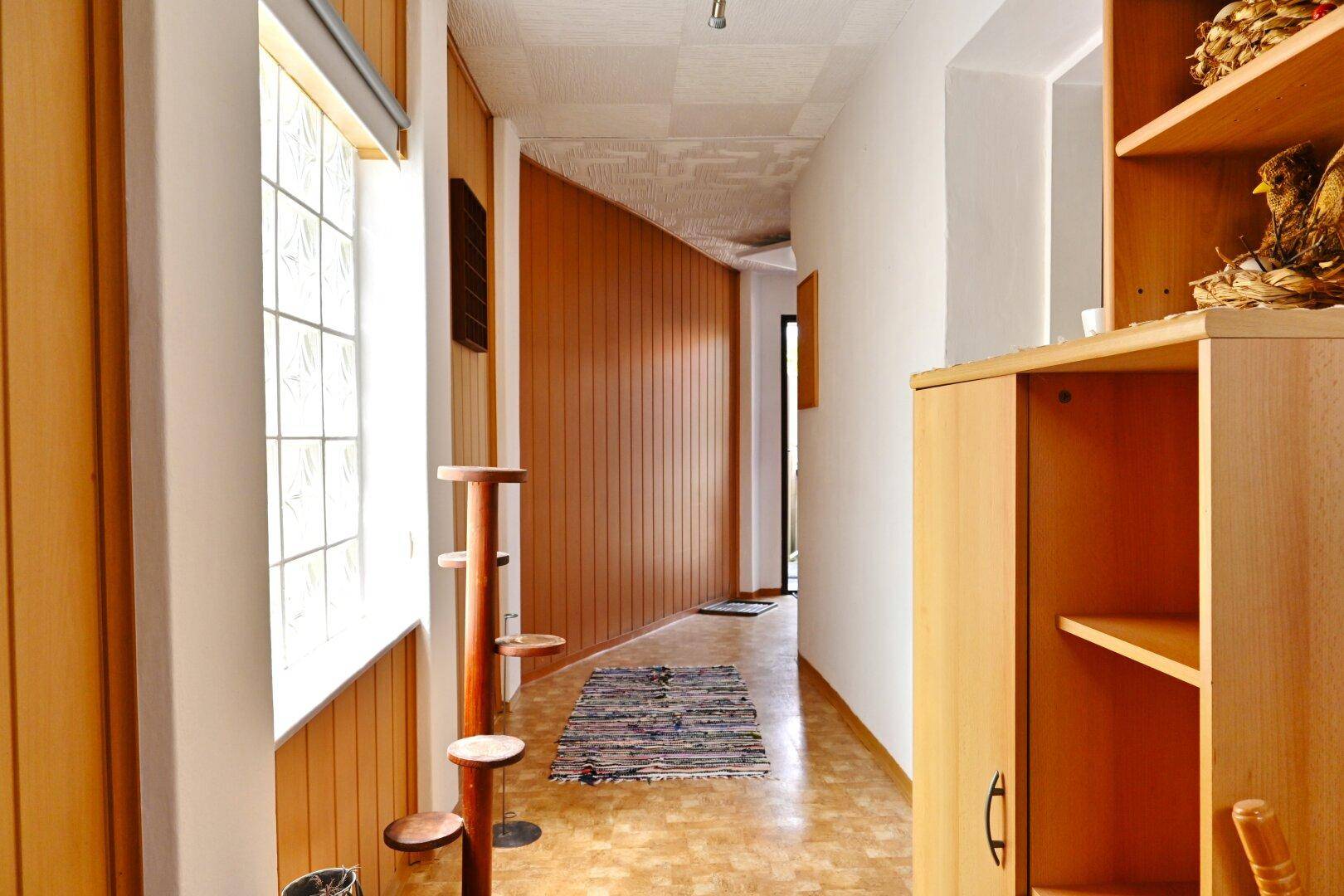 Langer Flur mit Holzverkleidung, Glasbausteinen und Teppichläufer.