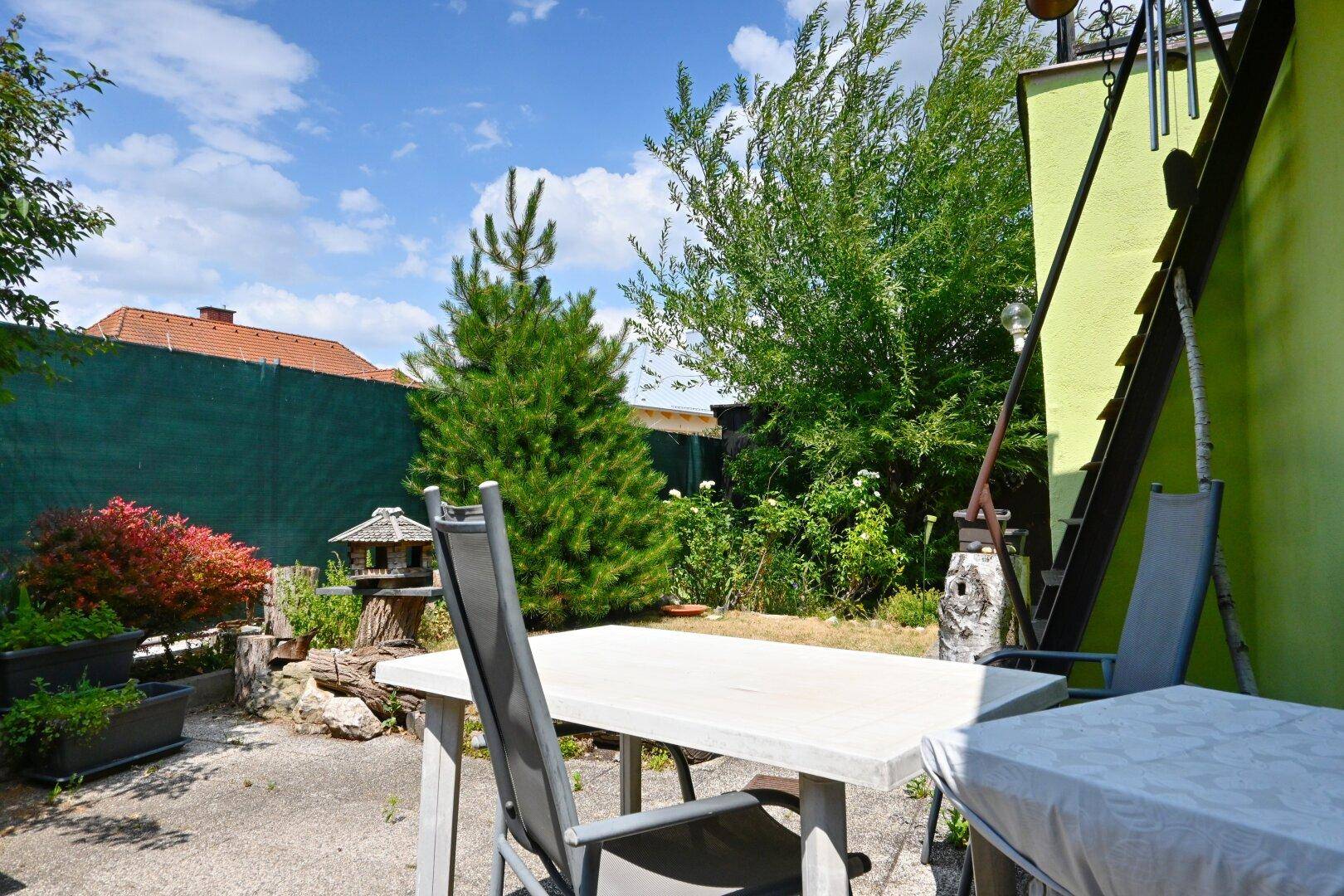 Gemütlicher Gartenbereich mit Sitzgelegenheiten, Bäumen und Vogelhaus.