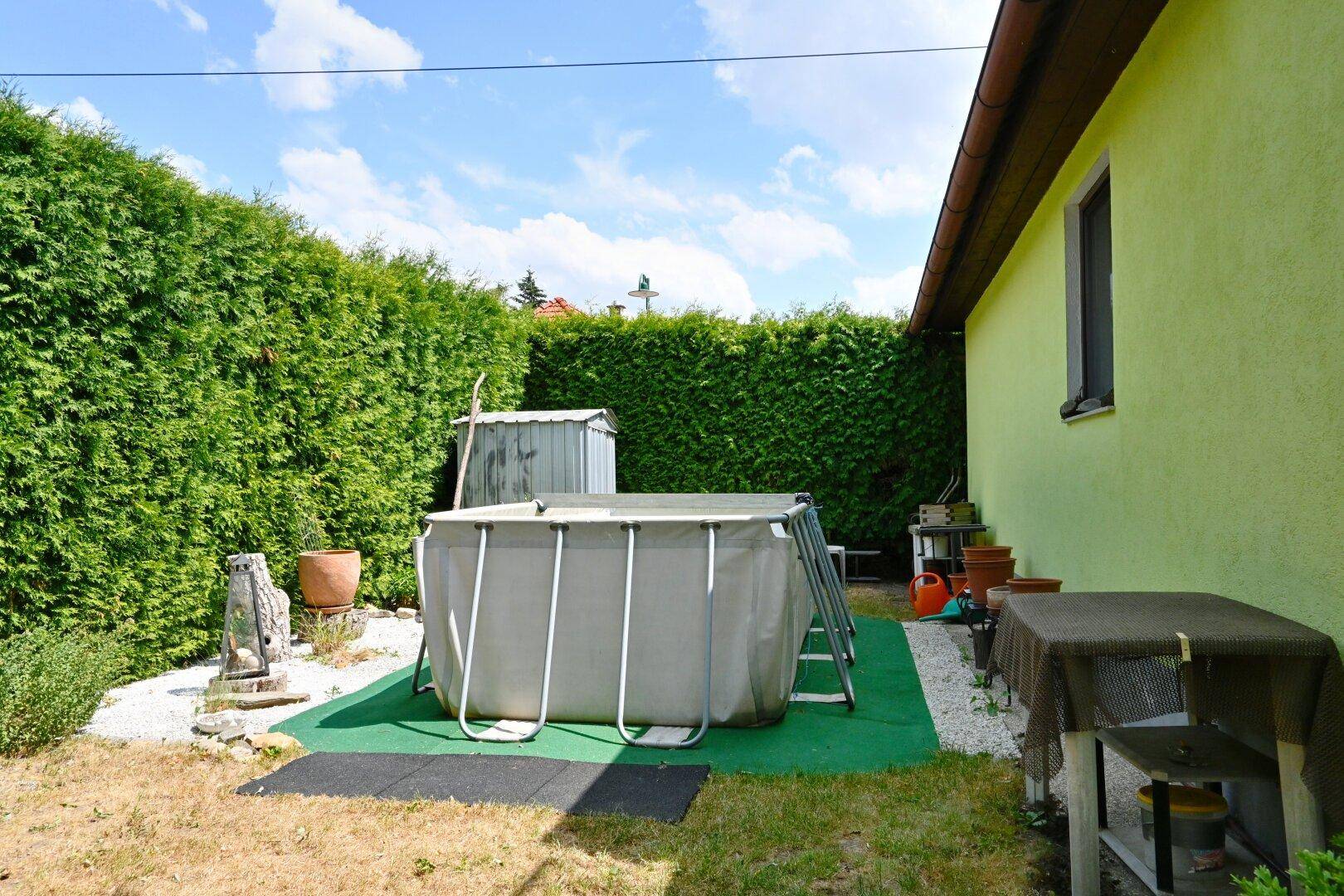 Gartenbereich mit Aufstellpool, Gartenhaus und hoher Hecke für Privatsphäre.