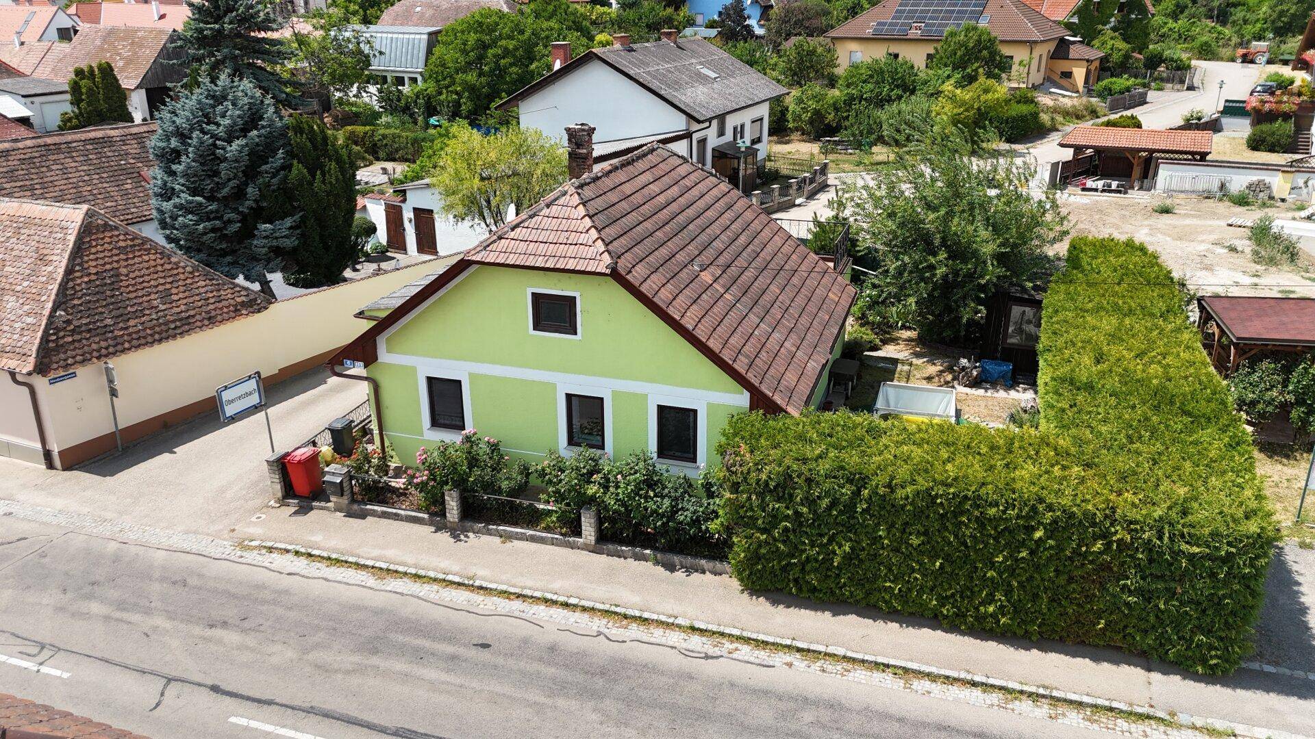 Luftaufnahme des grünen Hauses mit Satteldach, umgeben von Gärten und Nachbargebäuden.