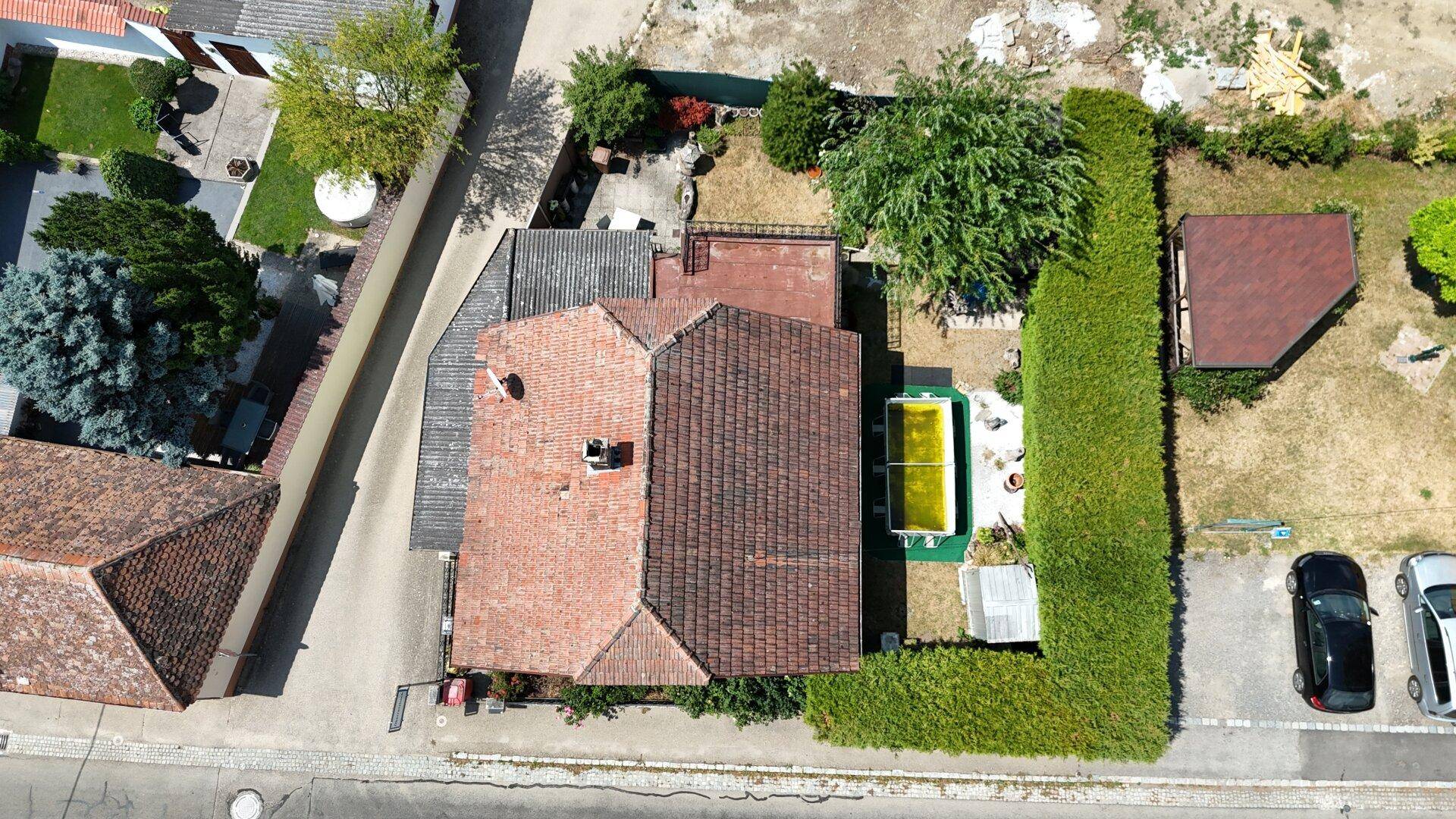 Luftaufnahme eines Hauses mit Ziegeldach, Garten, Pool und angrenzenden Parkplätzen.