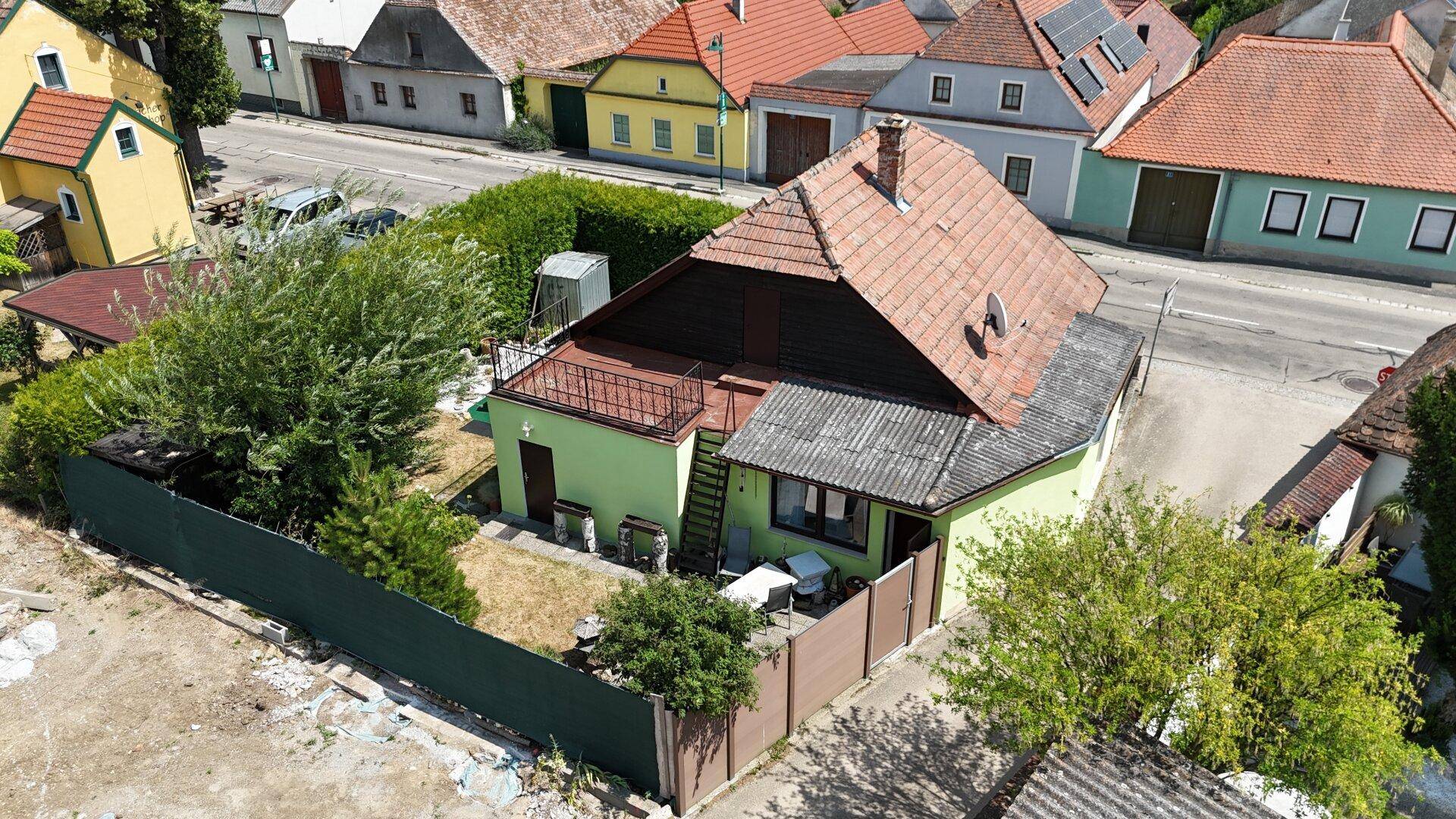 Luftaufnahme des grünen Hauses mit Satteldach, umgeben von Gärten und Nachbargebäuden.