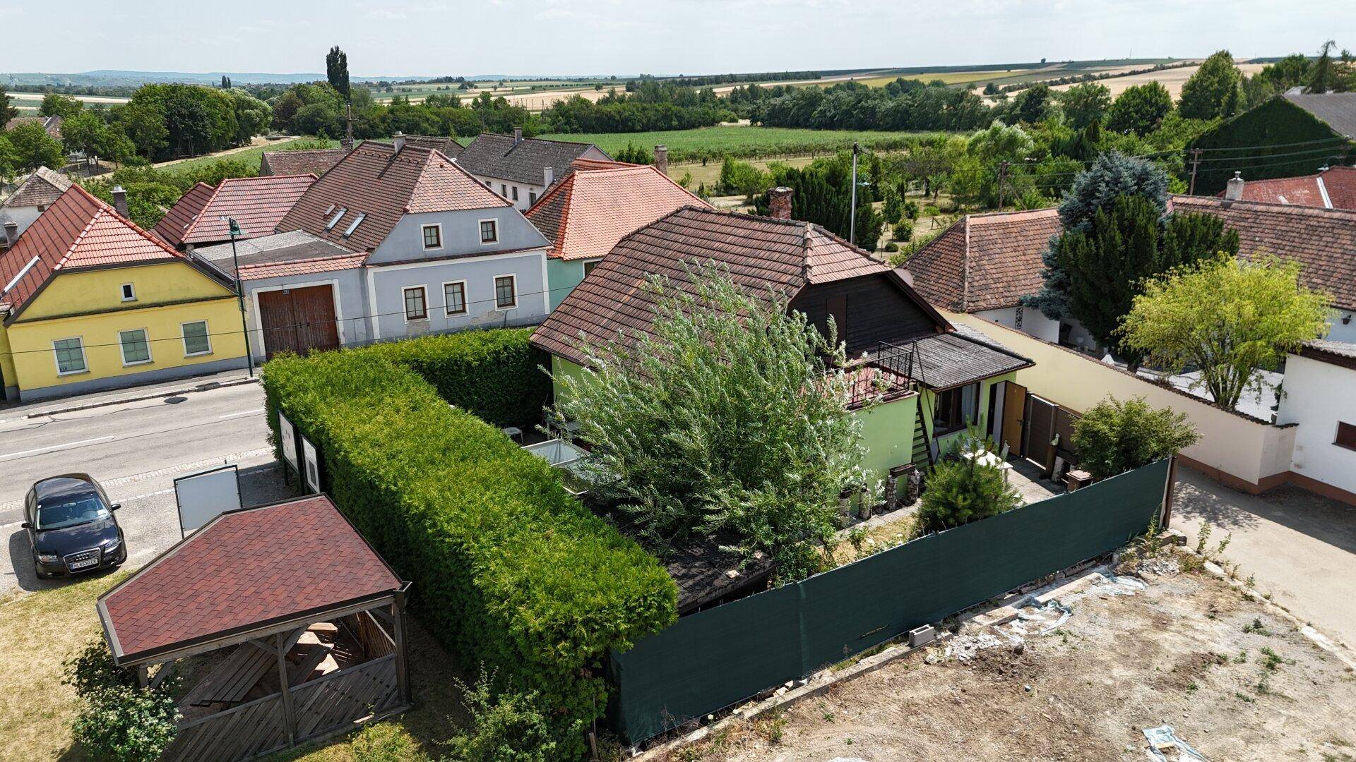 Blick auf ein Wohnhaus mit grüner Fassade, umgeben von Hecken und einer weiten ländlichen Landschaft.
