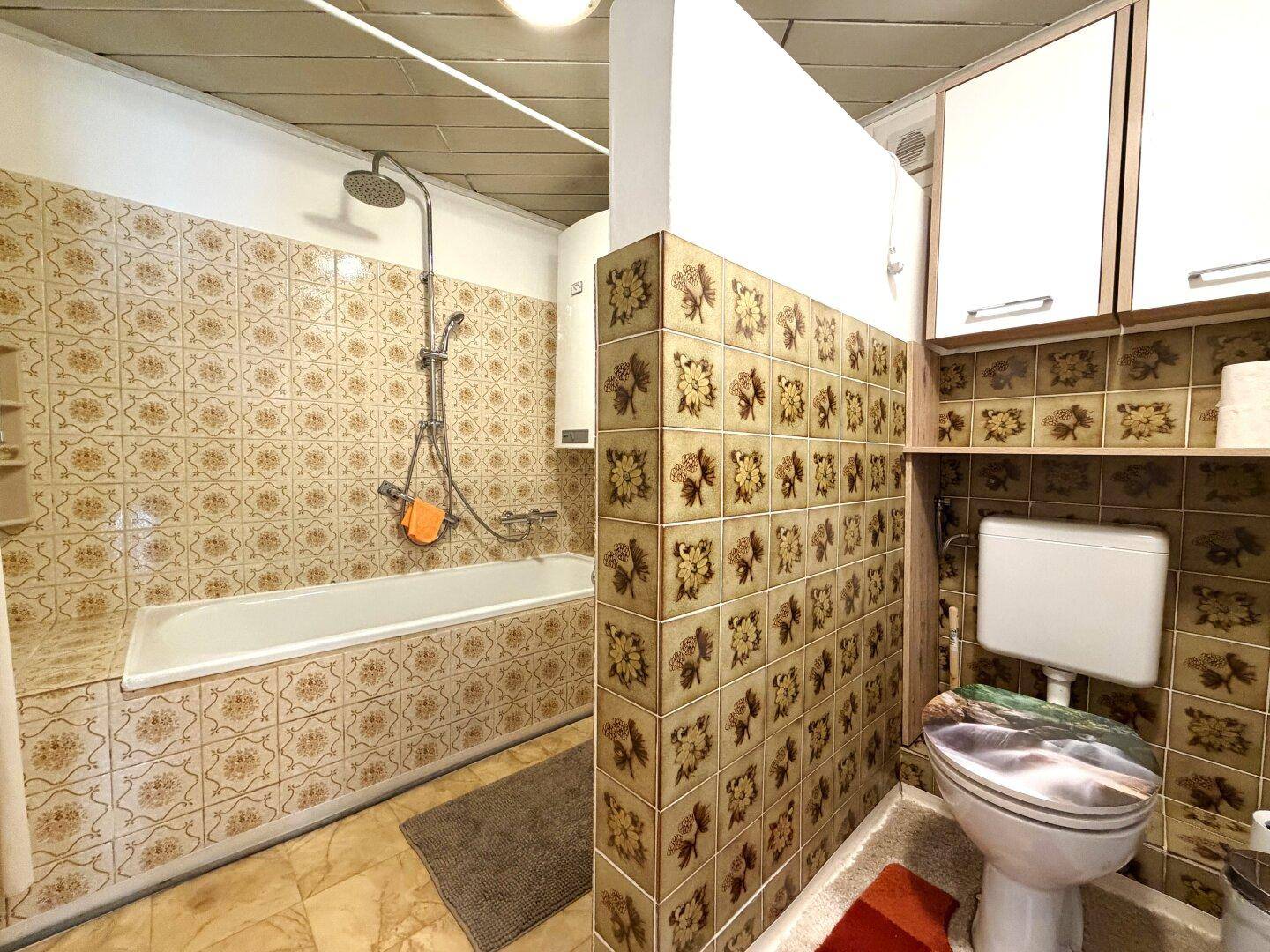 Badezimmer mit Badewanne, Dusche und gemusterten Fliesen im Retro-Stil.