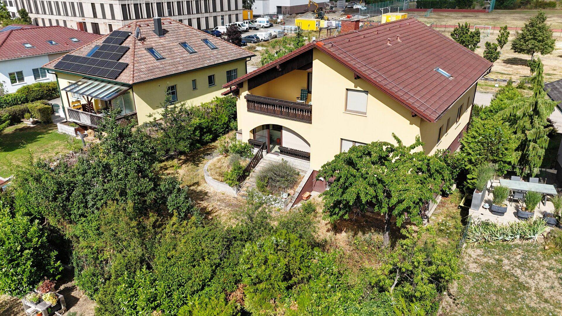 Weitläufige Luftaufnahme des Hauses mit Balkon, umgeben von viel Grün und Nachbargebäuden.