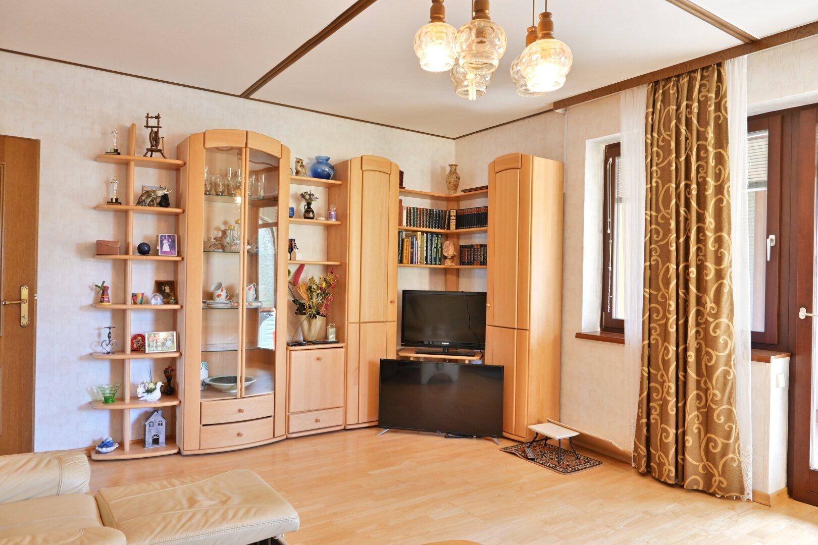 Wohnzimmer mit Holzmöbeln, Parkettboden und einem großen Fenster, das viel Licht hereinlässt.