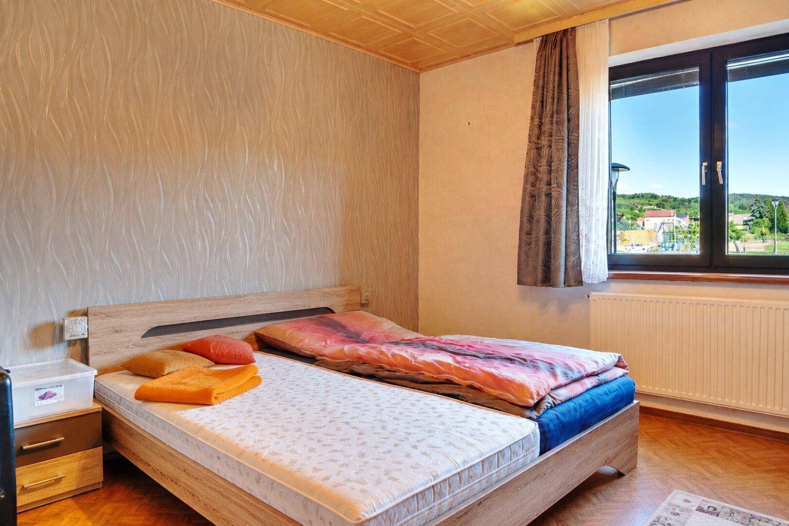 Schlafzimmer mit Doppelbett, Parkettboden und einem Fenster mit Blick ins Grüne.