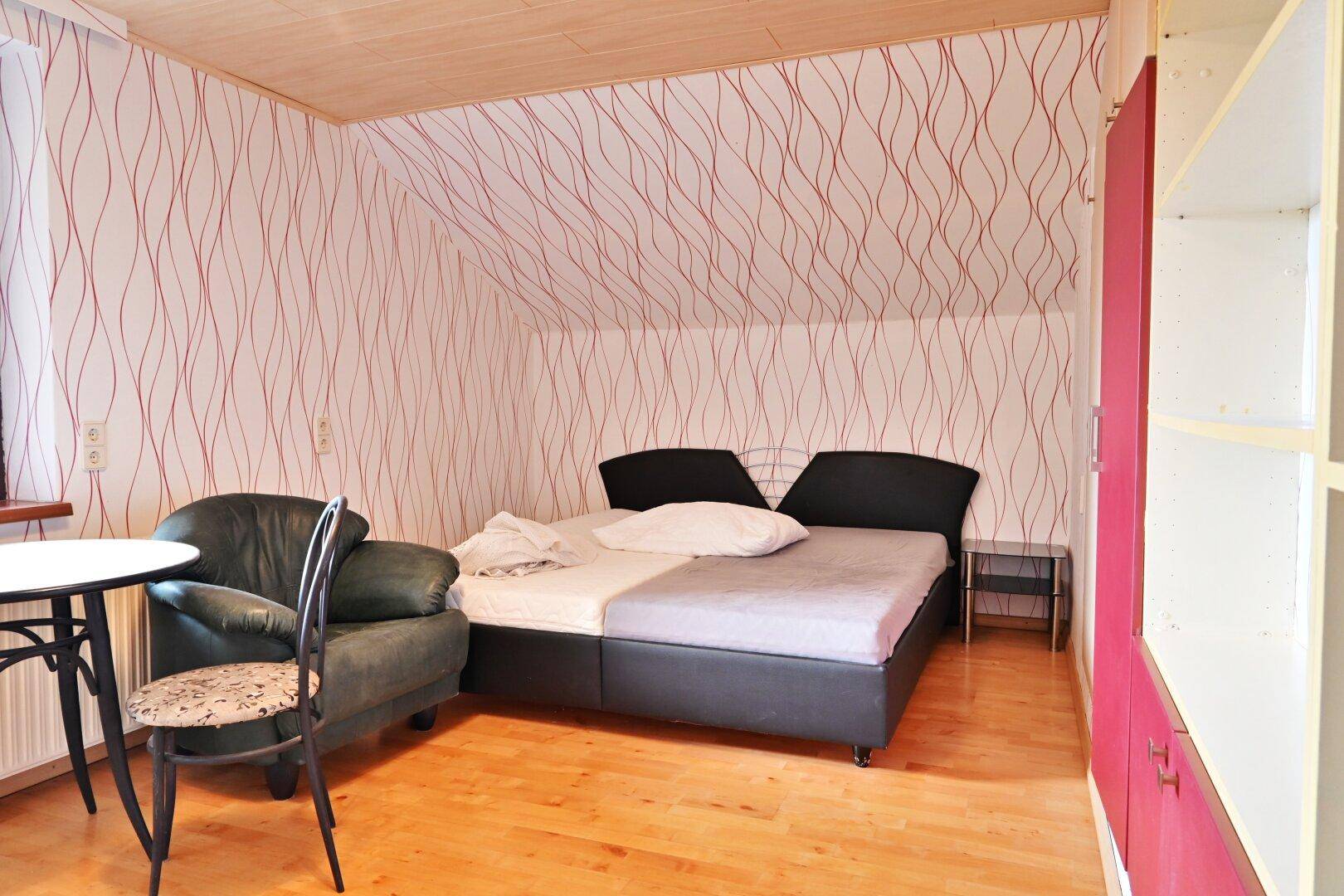 Schlafzimmer im Dachgeschoss mit gemusterter Tapete, Doppelbett und Holzboden.