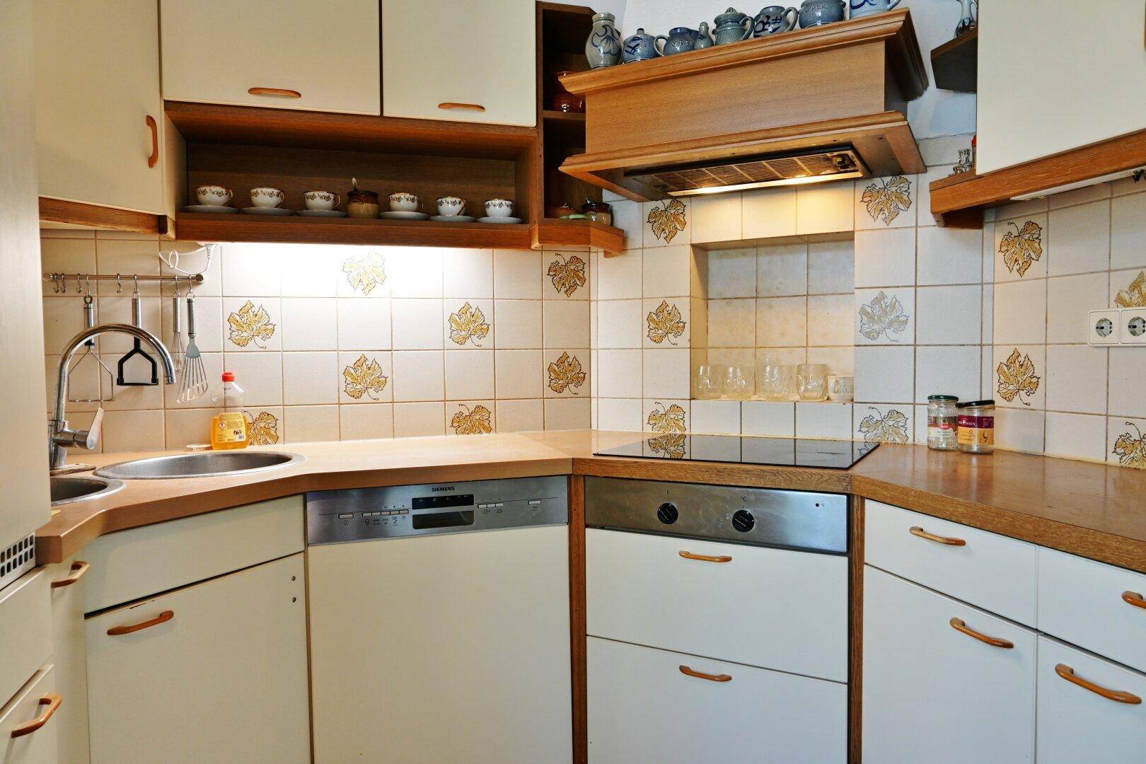 Funktionale Küche mit hellen Holzfronten, Fliesenrückwand und integriertem Geschirrspüler.