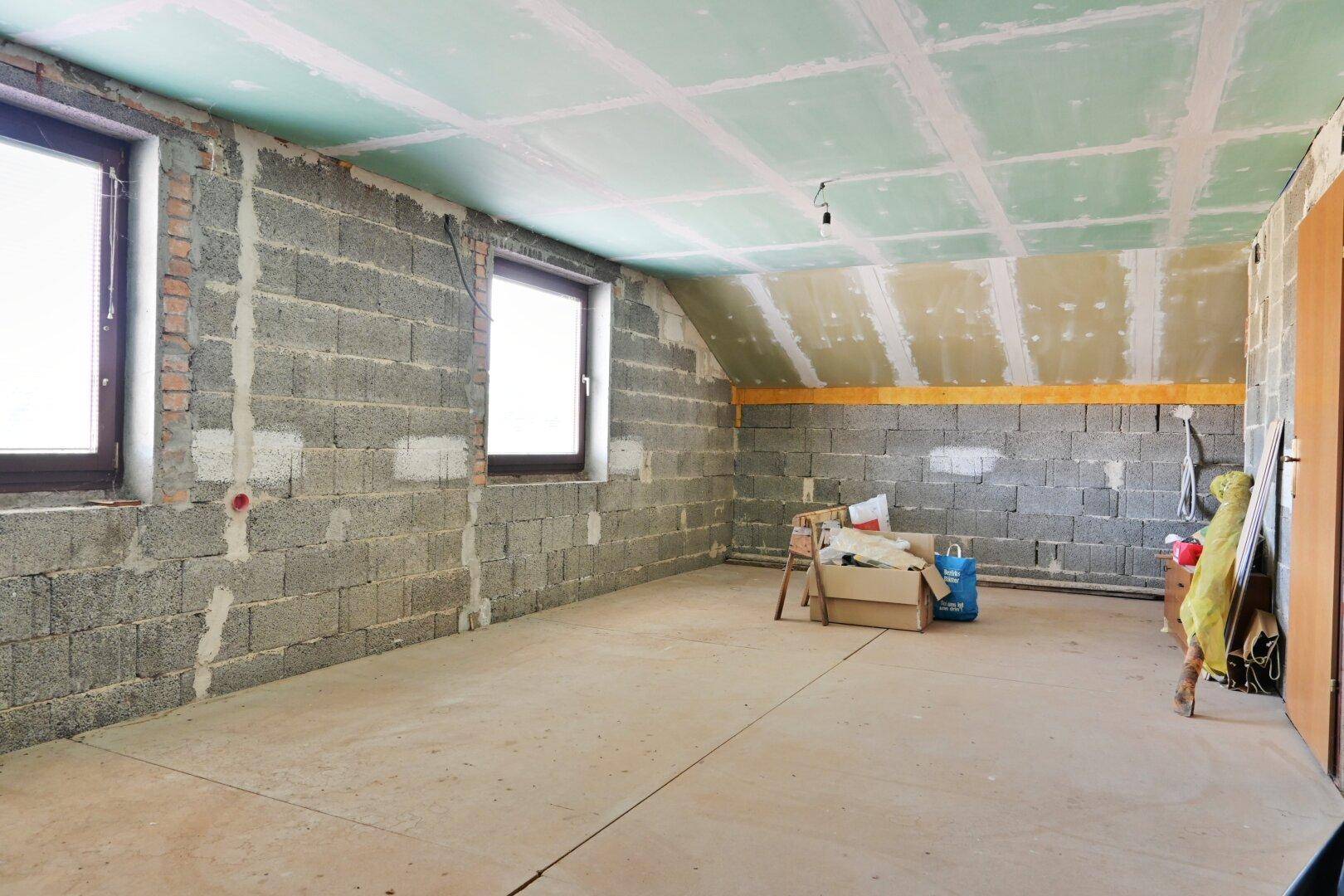 Unausgebauter Dachboden mit unverputzten Wänden und Fenstern, bereit für den Ausbau.