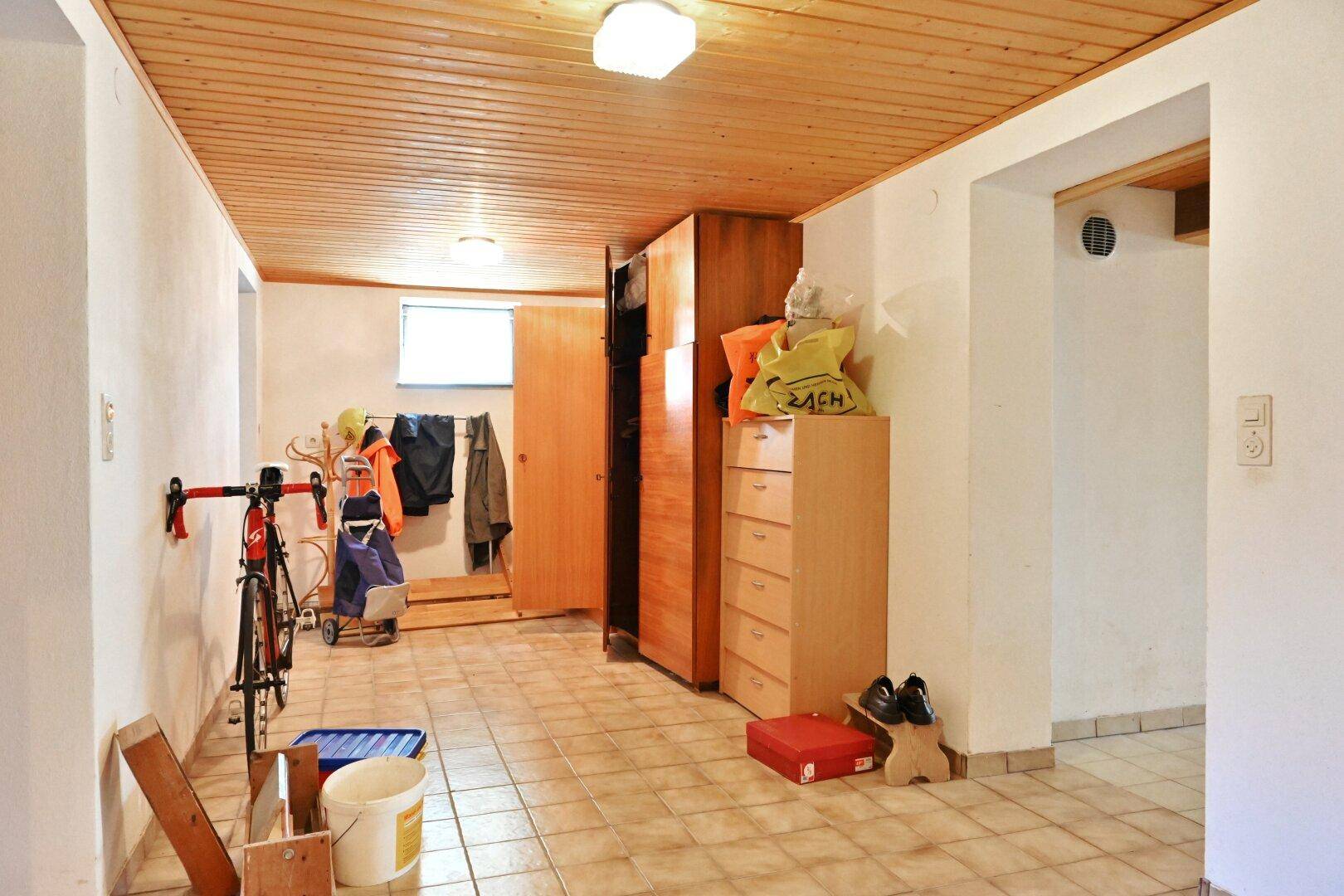 Geräumiger Kellerraum mit Fliesenboden, Holzdecke und Stauraum für Fahrräder und Haushaltsgegenstände.