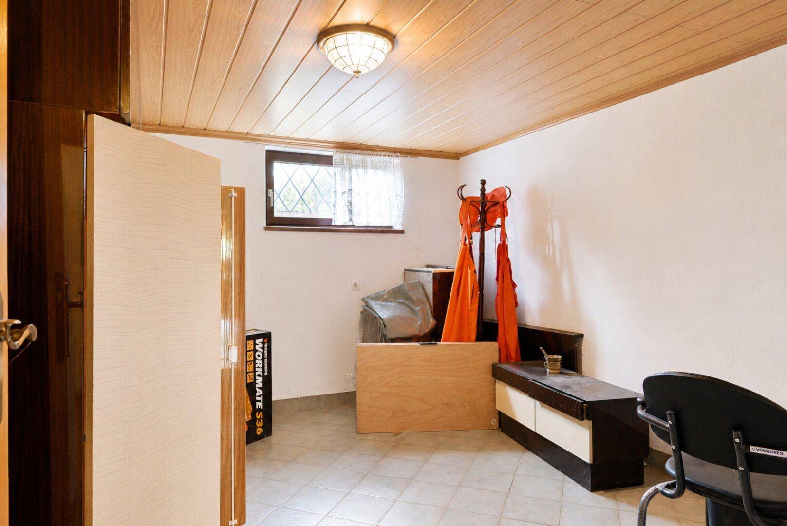 Kellerraum mit Holzdecke, Fliesenboden und kleinem Fenster, genutzt als Abstell- oder Hobbyraum.