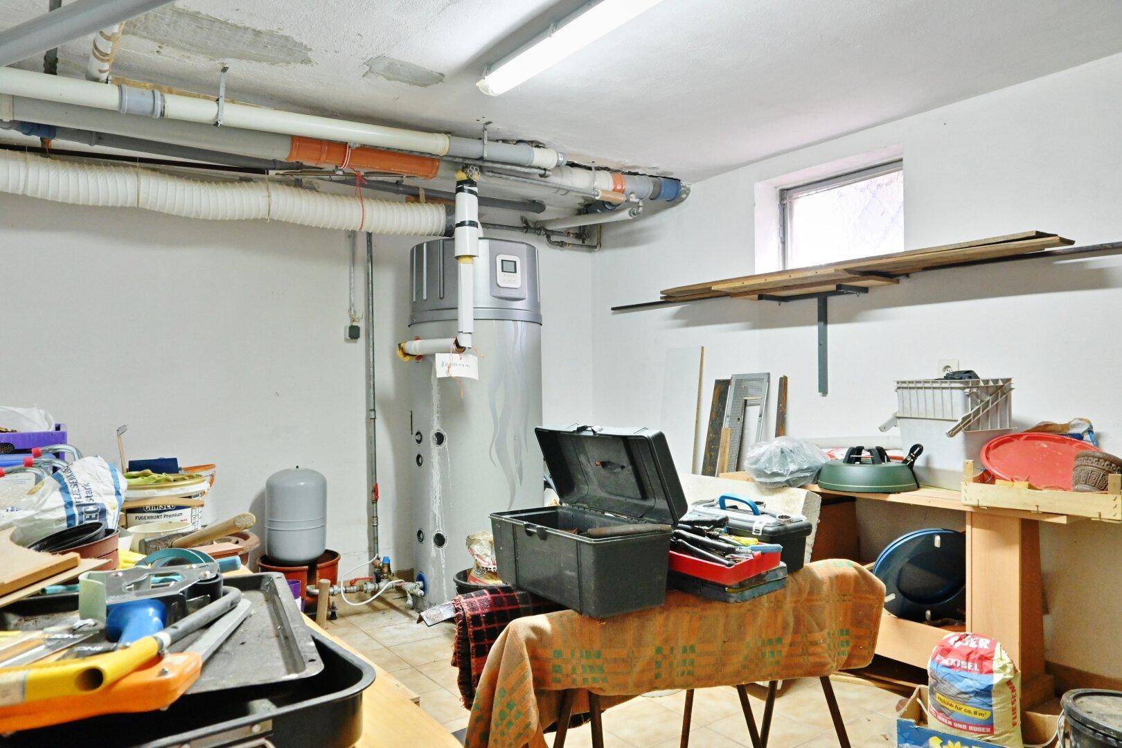 Technikraum im Keller mit Warmwasserspeicher, sichtbaren Rohren und Werkzeugen.