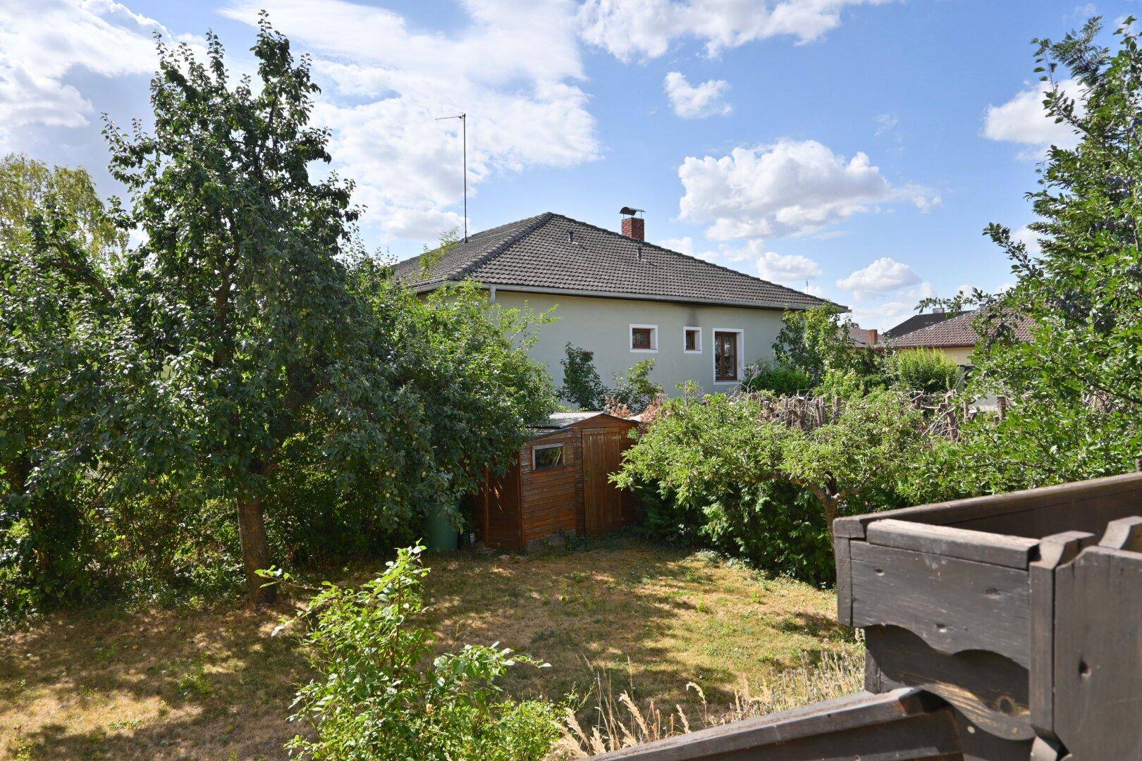 Gartenansicht mit Rasenfläche, Bäumen und einem kleinen Gartenhaus, vom Balkon aus gesehen.