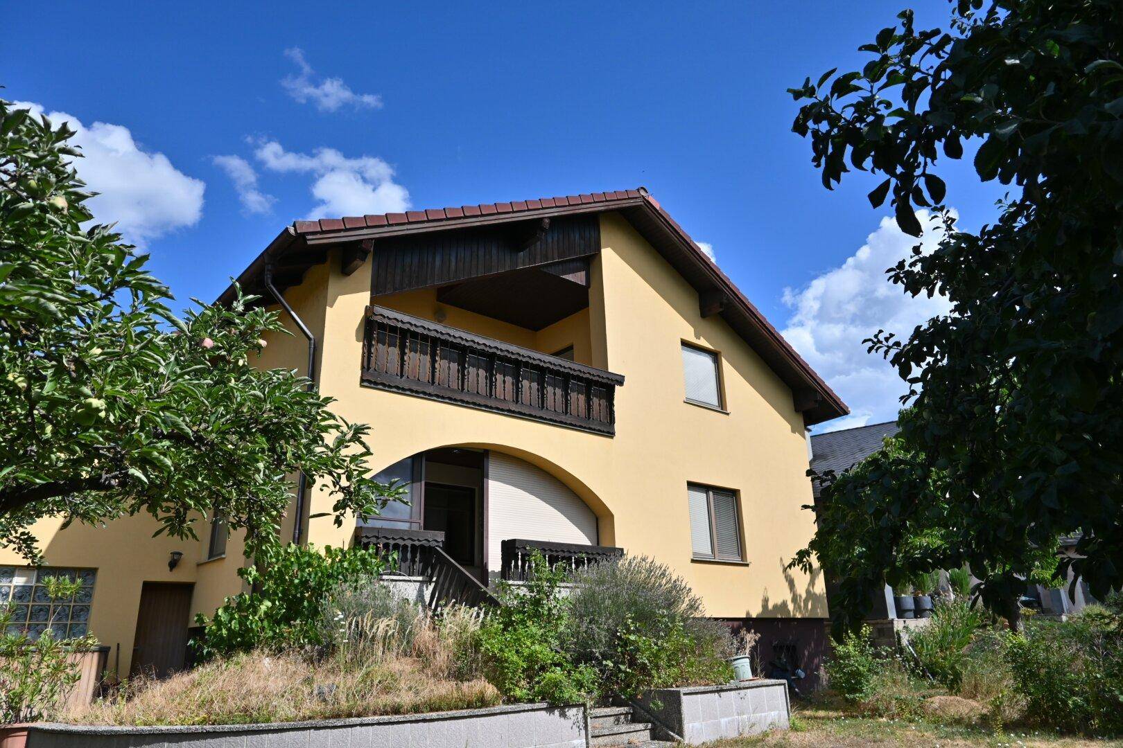 Seitenansicht des Hauses mit einem überdachten Balkon und einem kleinen Gartenbereich.
