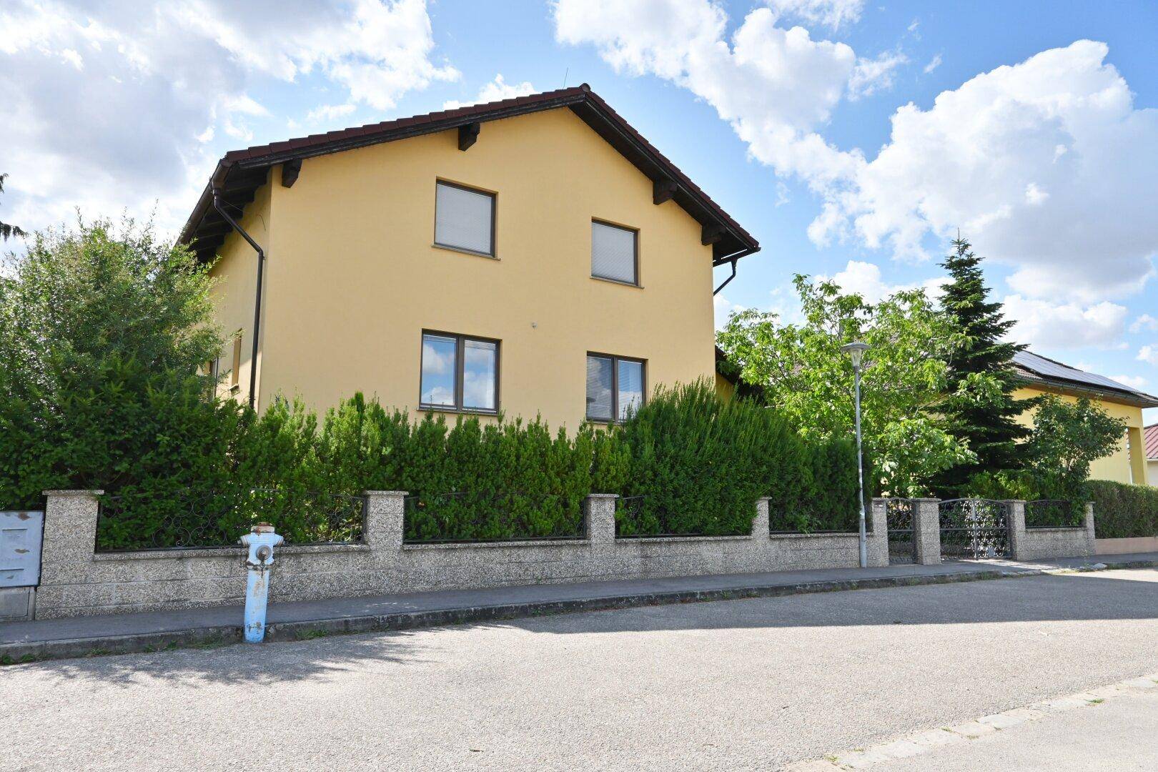 Straßenansicht des gelben Einfamilienhauses mit gepflegter Hecke und Zaun.