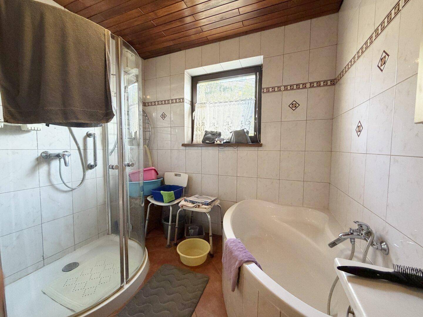 Badezimmer mit Eckbadewanne, Duschkabine und Holzdecke, hell gefliest.