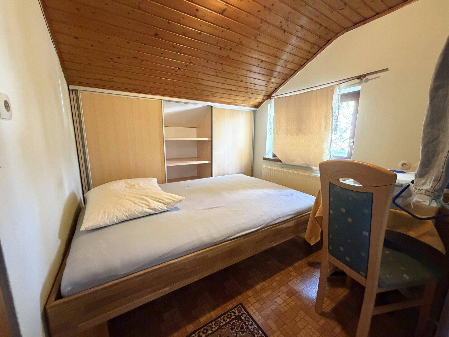 Schlafzimmer mit Holzbett, Einbauschrank und schräger Decke, typisch für Dachgeschoss.