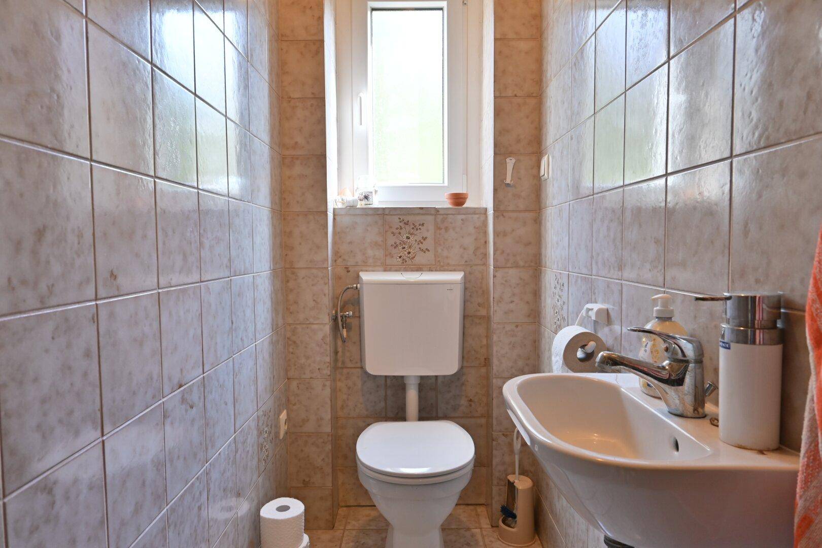 Kleines Gäste-WC mit Fenster, Wand-WC und Waschbecken, komplett gefliest.