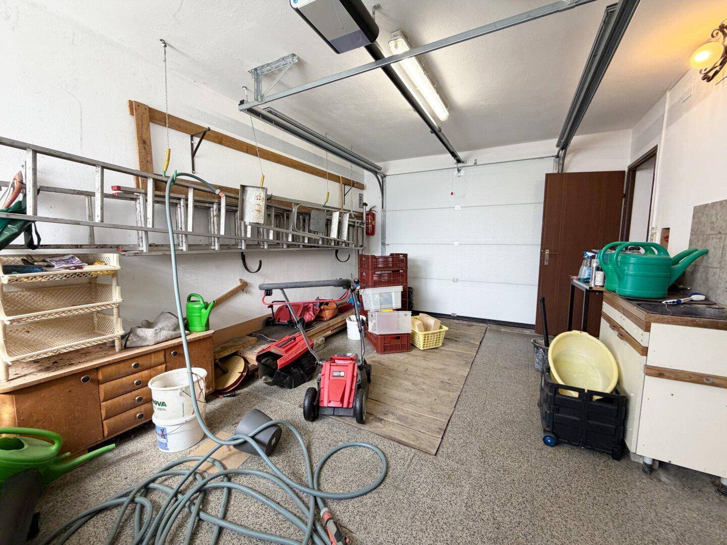 Geräumige Garage mit automatischem Tor, genutzt als Abstellraum für Werkzeuge und Gartengeräte.