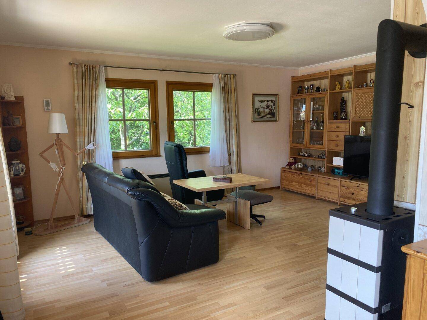 Gemütliches Wohnzimmer mit Holzboden, Kaminofen und Blick ins Grüne.