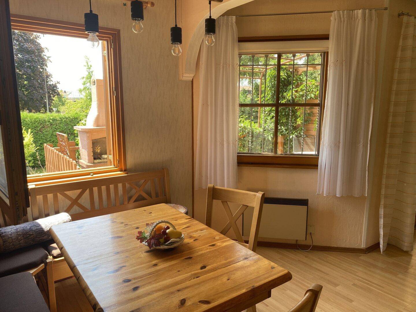Essbereich mit rustikalem Holztisch und Bänken, hell durch große Fenster.
