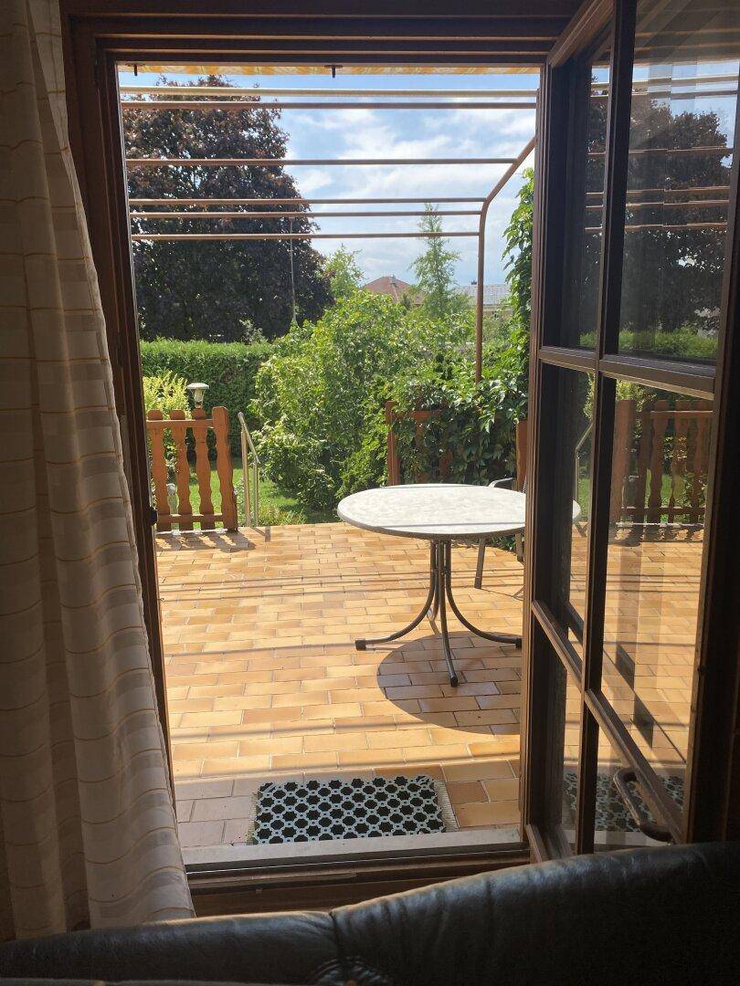 Blick vom Innenraum durch die Terrassentür auf die sonnige Terrasse und den Garten.