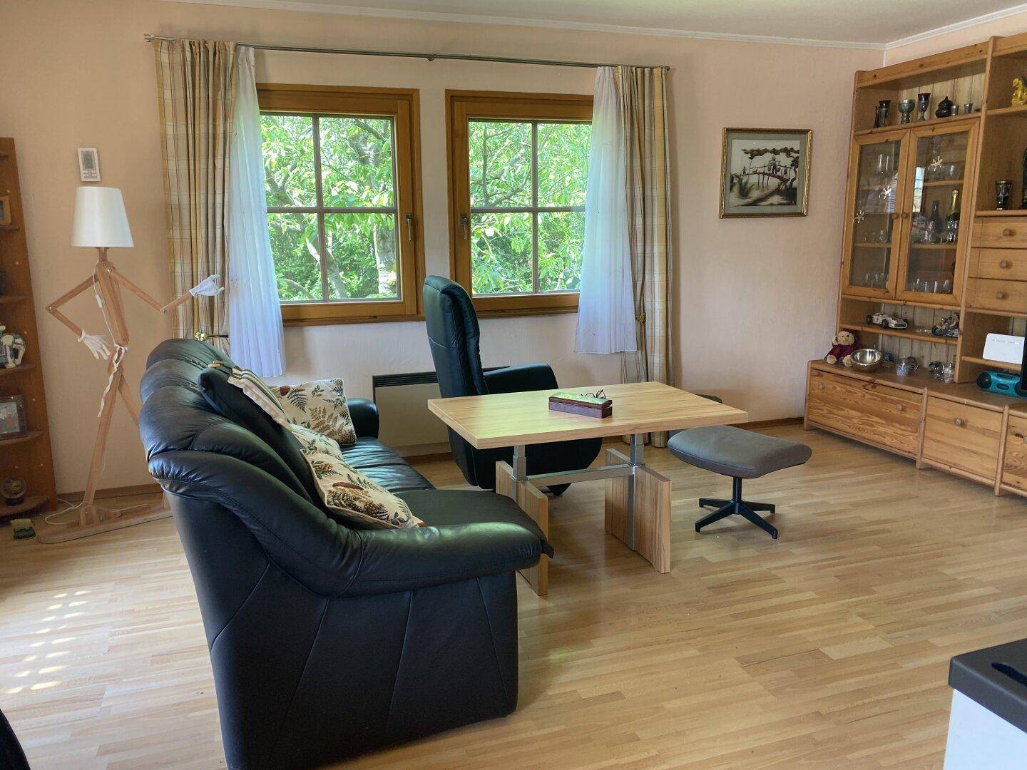 Geräumiges Wohnzimmer mit bequemer Couch, Holzboden und Blick ins Grüne.