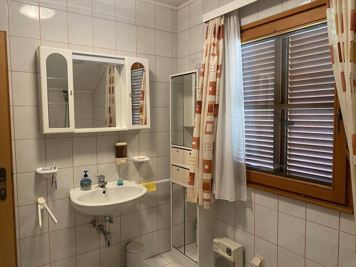Badezimmer mit Waschbecken, Spiegelschrank und hellen Fliesen.