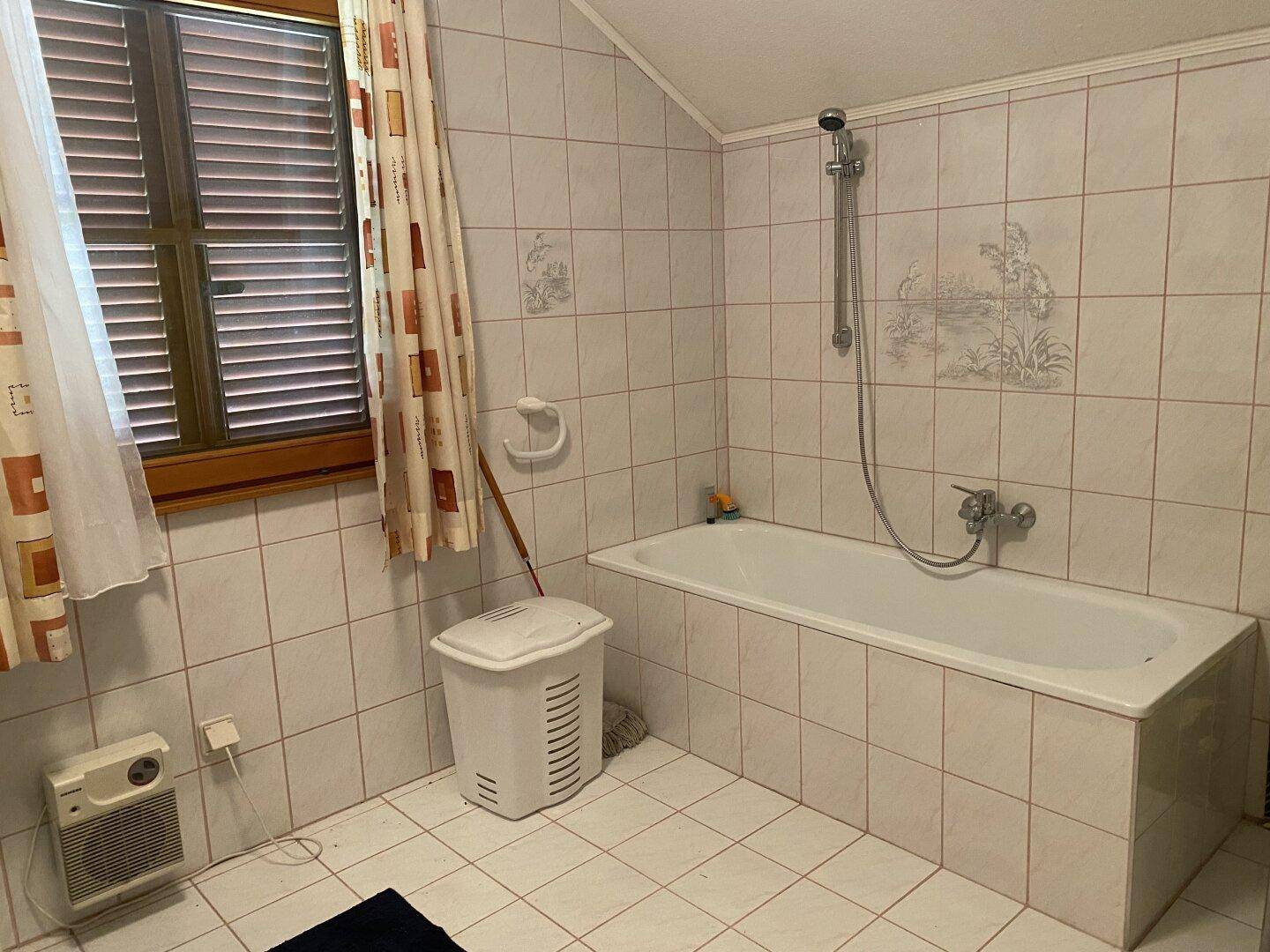 Badezimmer mit Badewanne, Duschvorrichtung und hell gefliesten Wänden.