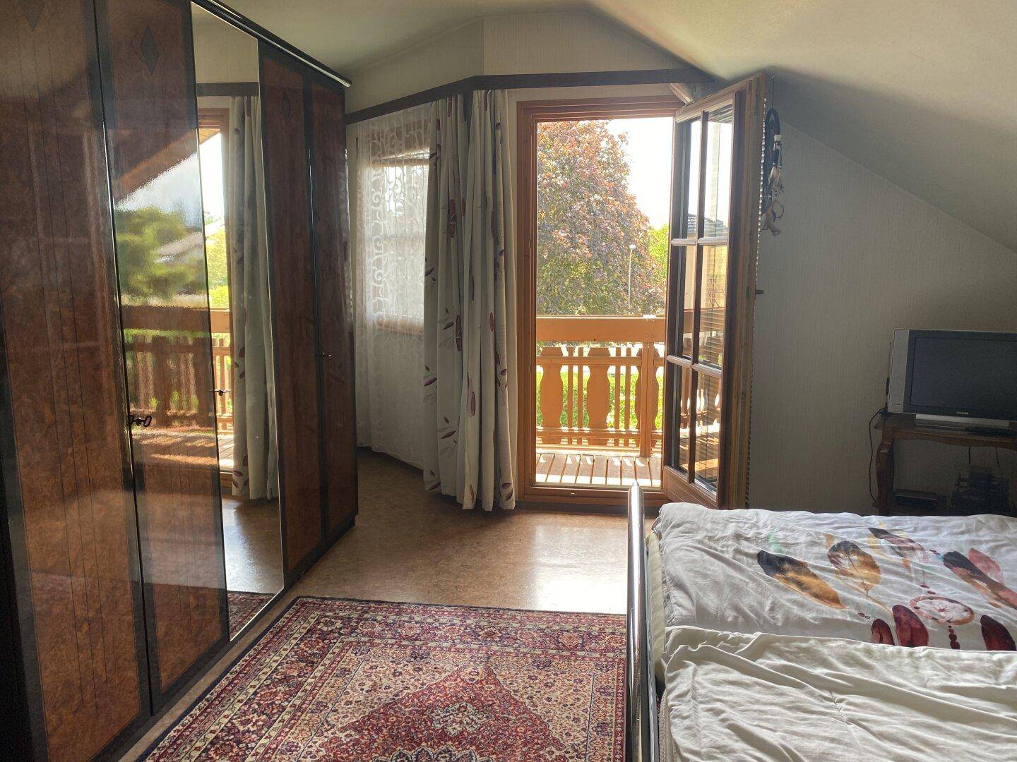 Schlafzimmer im Dachgeschoss mit Spiegelschrank und Zugang zum Balkon.