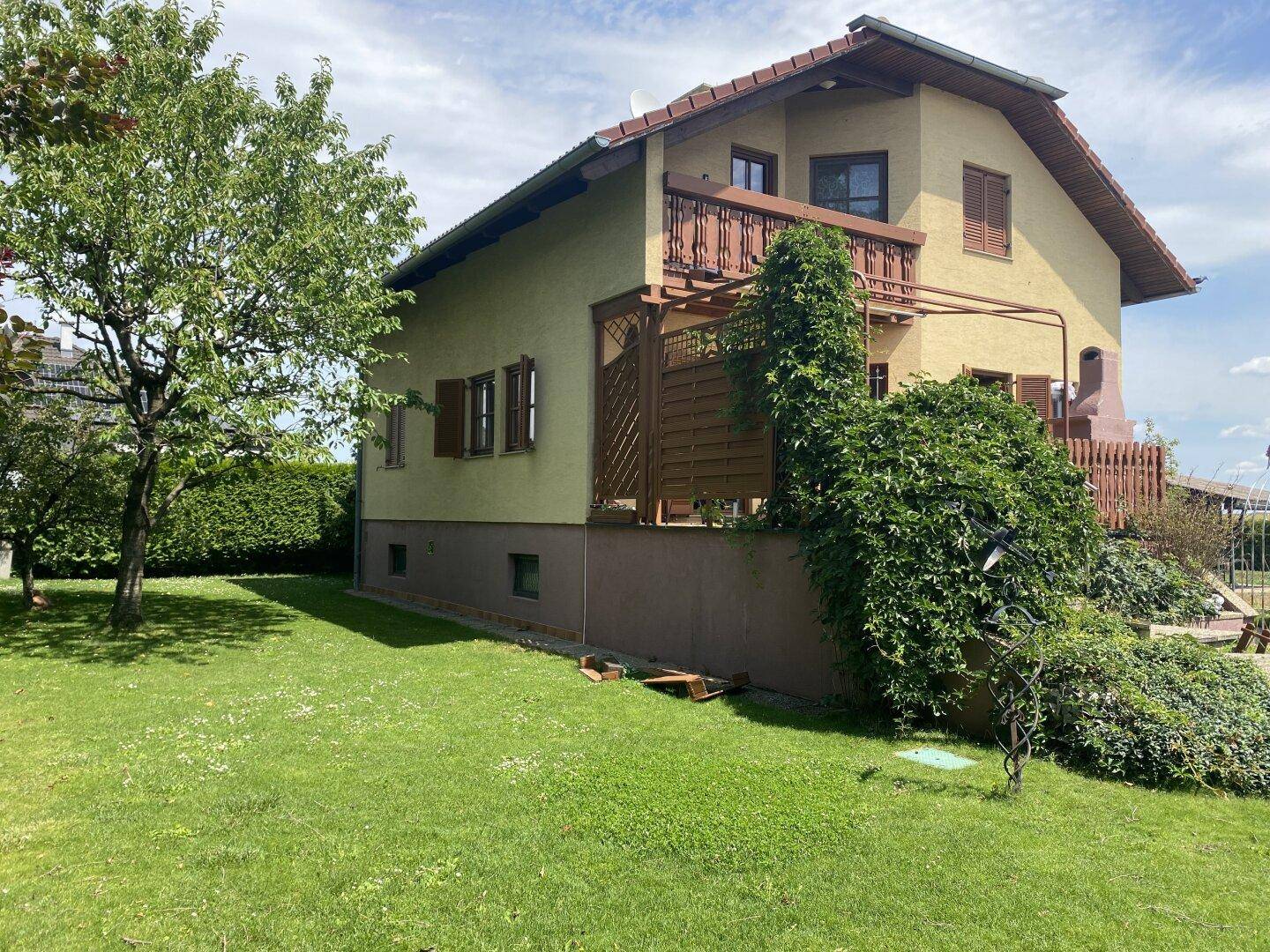 Hausfassade mit Balkon und Terrasse, umgeben von einem gepflegten grünen Garten.
