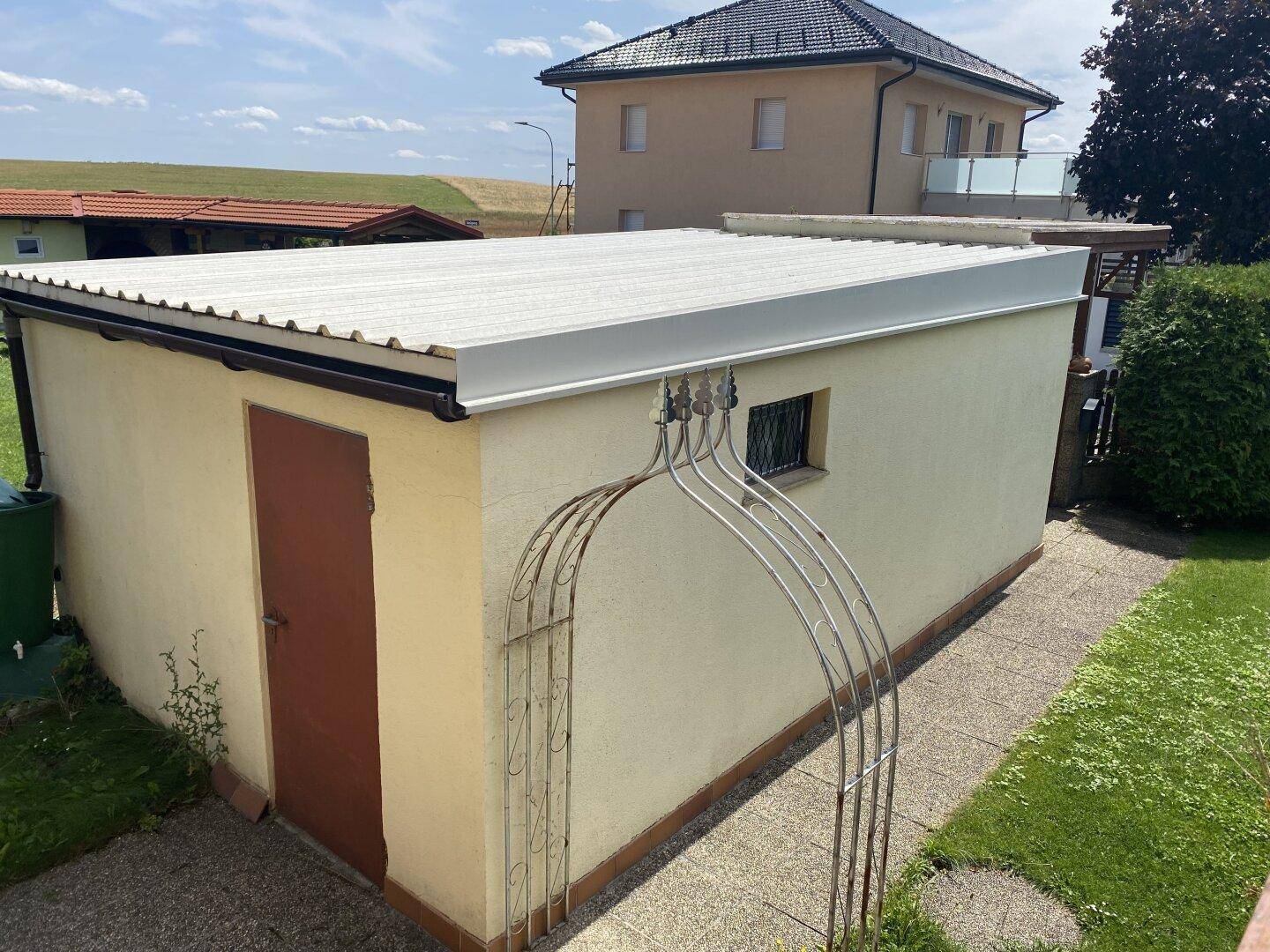 Kleines Nebengebäude mit Wellblechdach und einem Bogen im Gartenbereich.