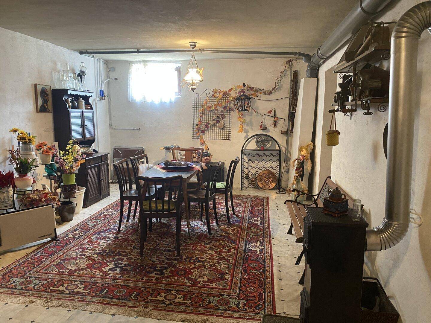 Rustikaler Kellerraum mit Esstisch, Teppich und einem Holzofen für gemütliche Abende.