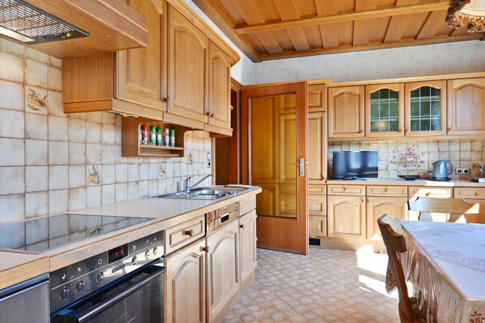 Helle Küche mit Holzschränken, integrierten Geräten und Essbereich am Fenster.