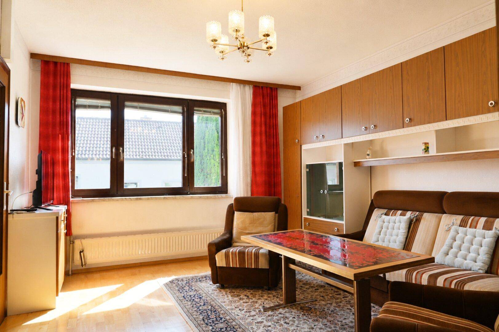 Gemütliches Wohnzimmer mit Holzmöbeln, Teppich und Blick ins Grüne.