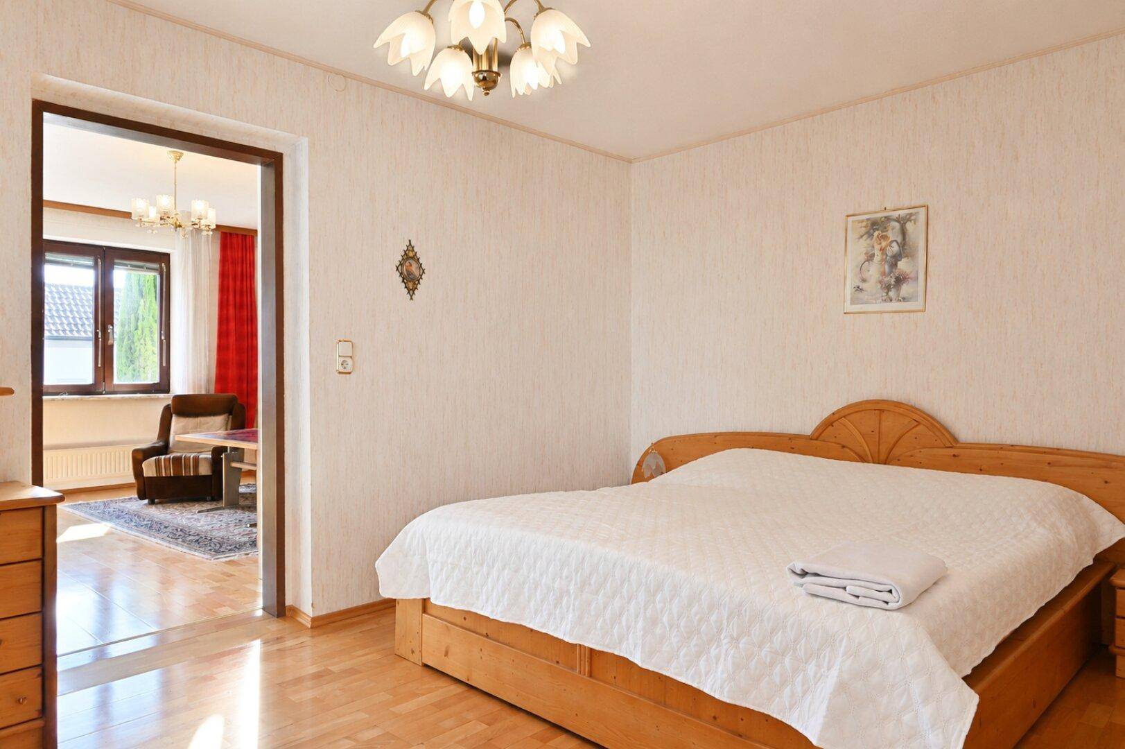Helles Schlafzimmer mit Holzbett und Zugang zum Wohnbereich.