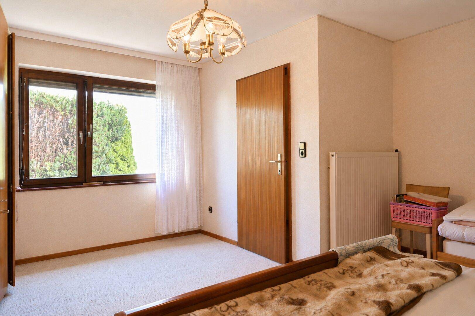 Schlafzimmer mit Teppichboden, Holzbett und Fenster mit Blick ins Grüne.