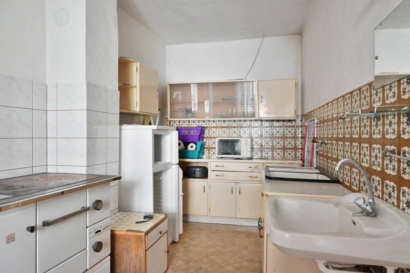 Ältere Küche mit traditionellen Fliesen, Spüle und freistehendem Kühlschrank.