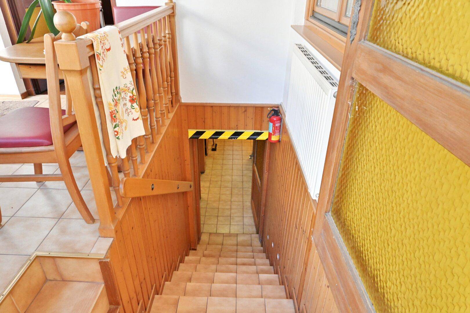 Treppenabgang zum Keller mit Holzgeländer und Fliesenboden.