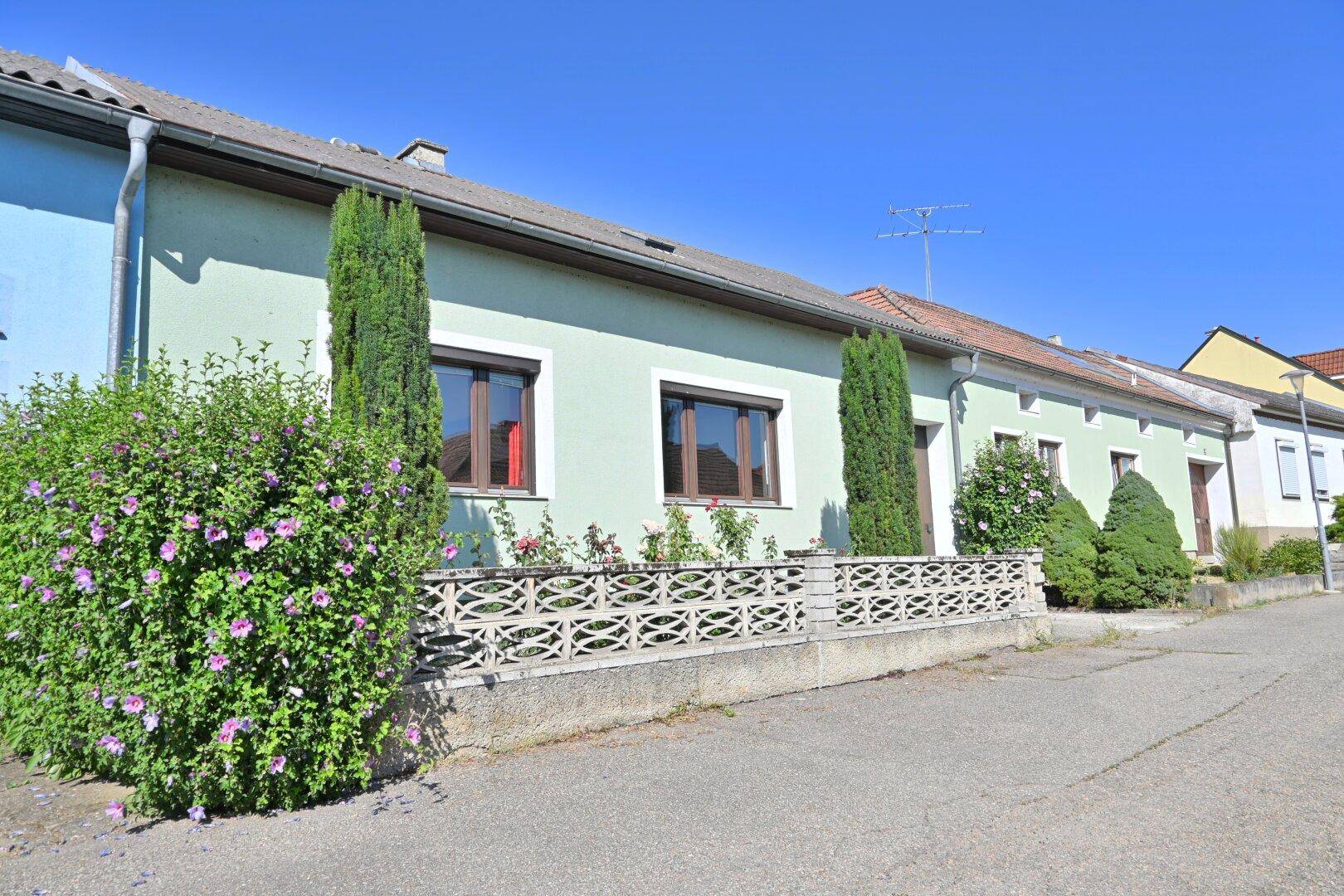 Ansicht der Hausfassade mit Vorgarten und Straße an einem sonnigen Tag.