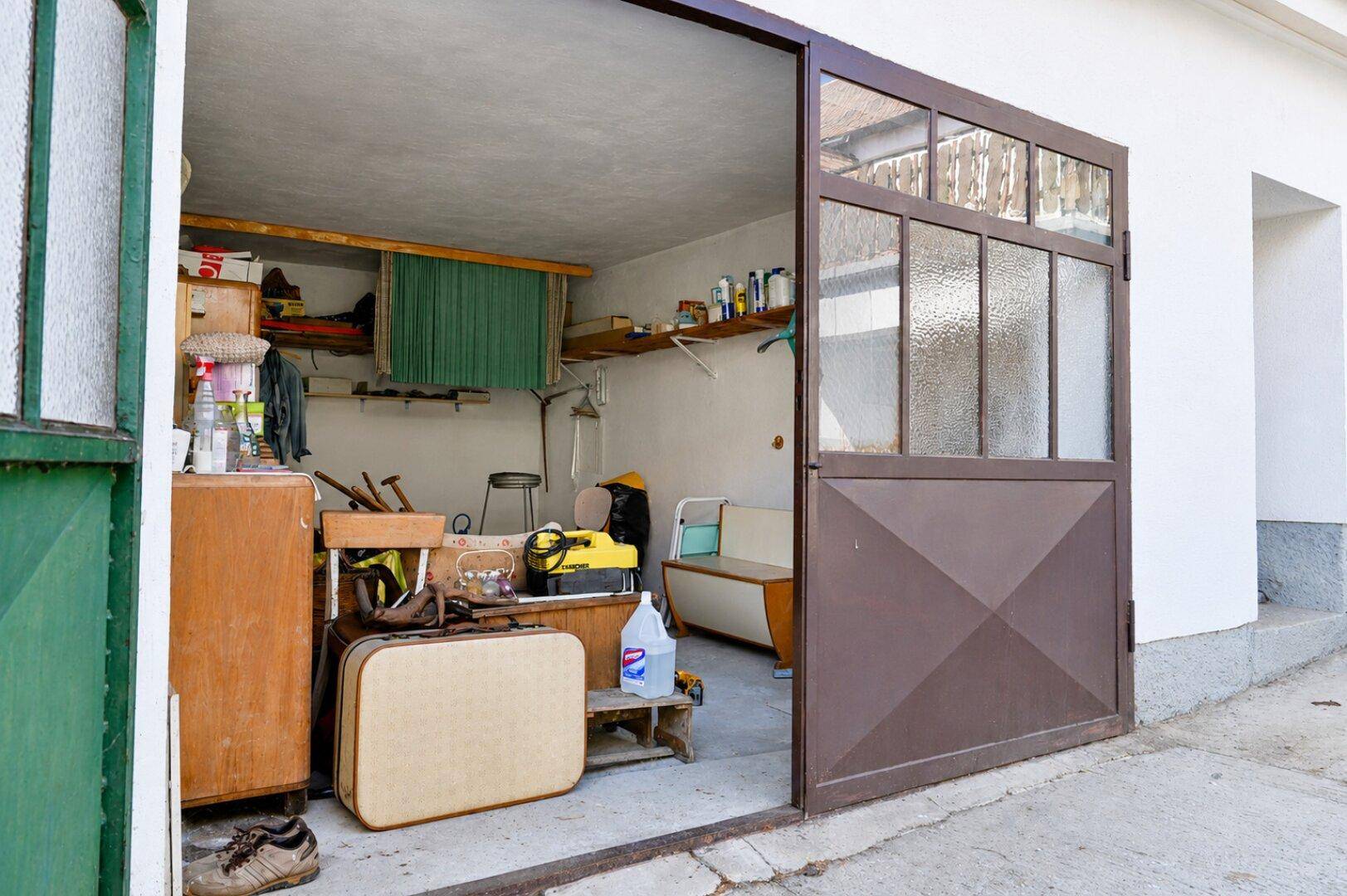 Offene Garage mit Lagerfläche und verschiedenen Gegenständen.