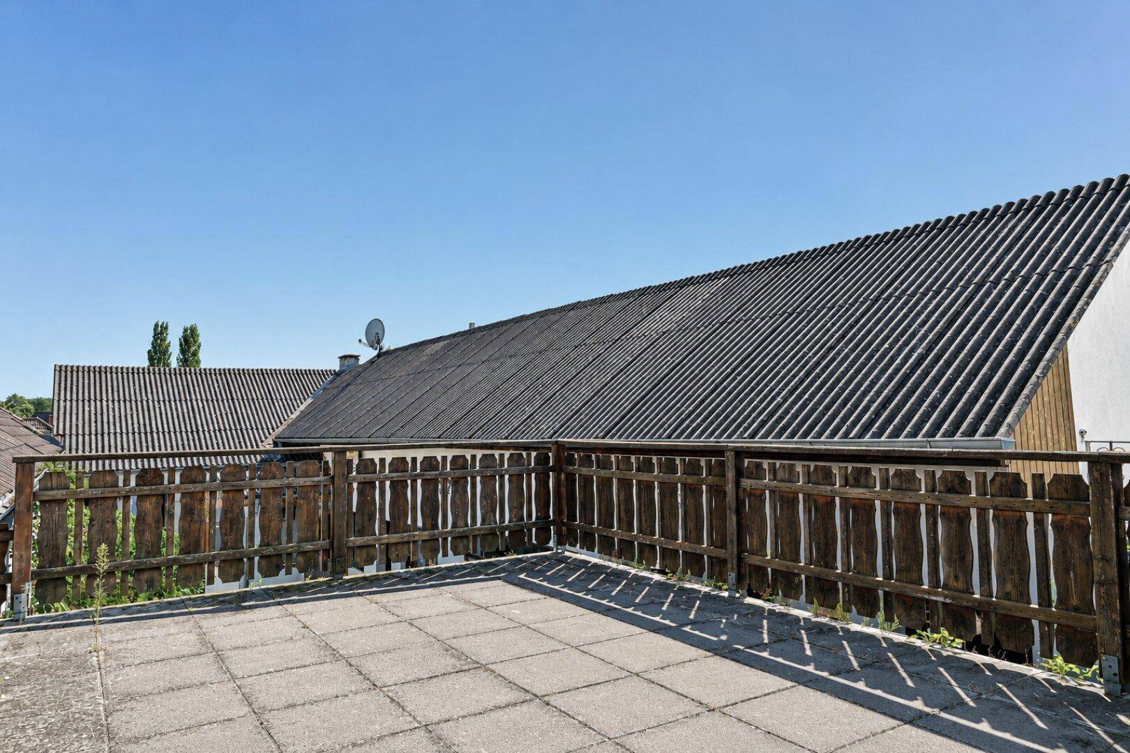 Große gepflasterte Terrasse mit Holzzaun und Blick auf die umliegenden Dächer.