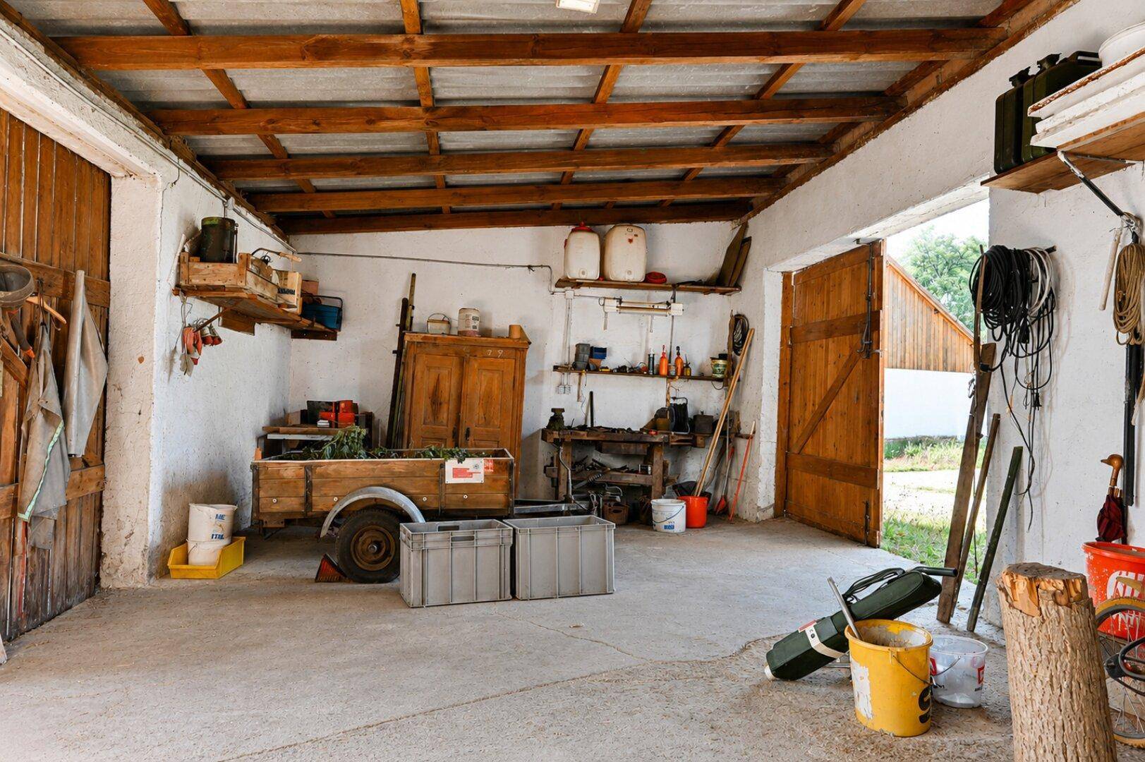 Geräumige Werkstatt mit Holzbalkendecke, Werkzeugen und einem kleinen Anhänger.