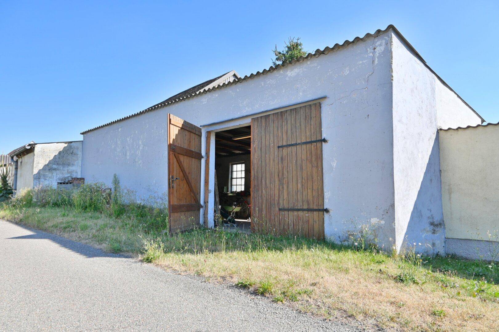 Einfaches Nebengebäude mit großen Holztüren und Wellblechdach in ländlicher Umgebung.