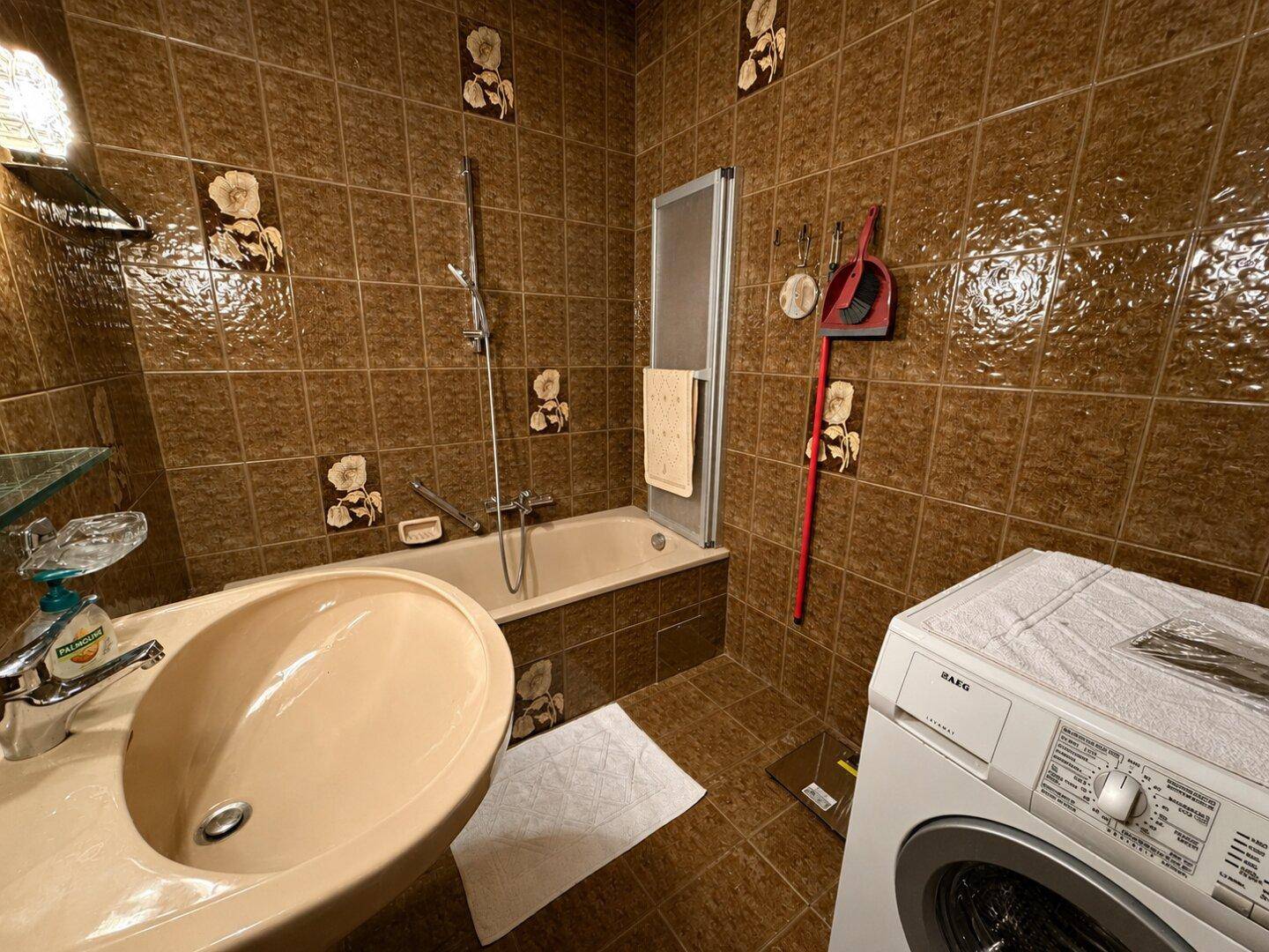 Badezimmer mit braunen Fliesen, Badewanne und Waschmaschine.