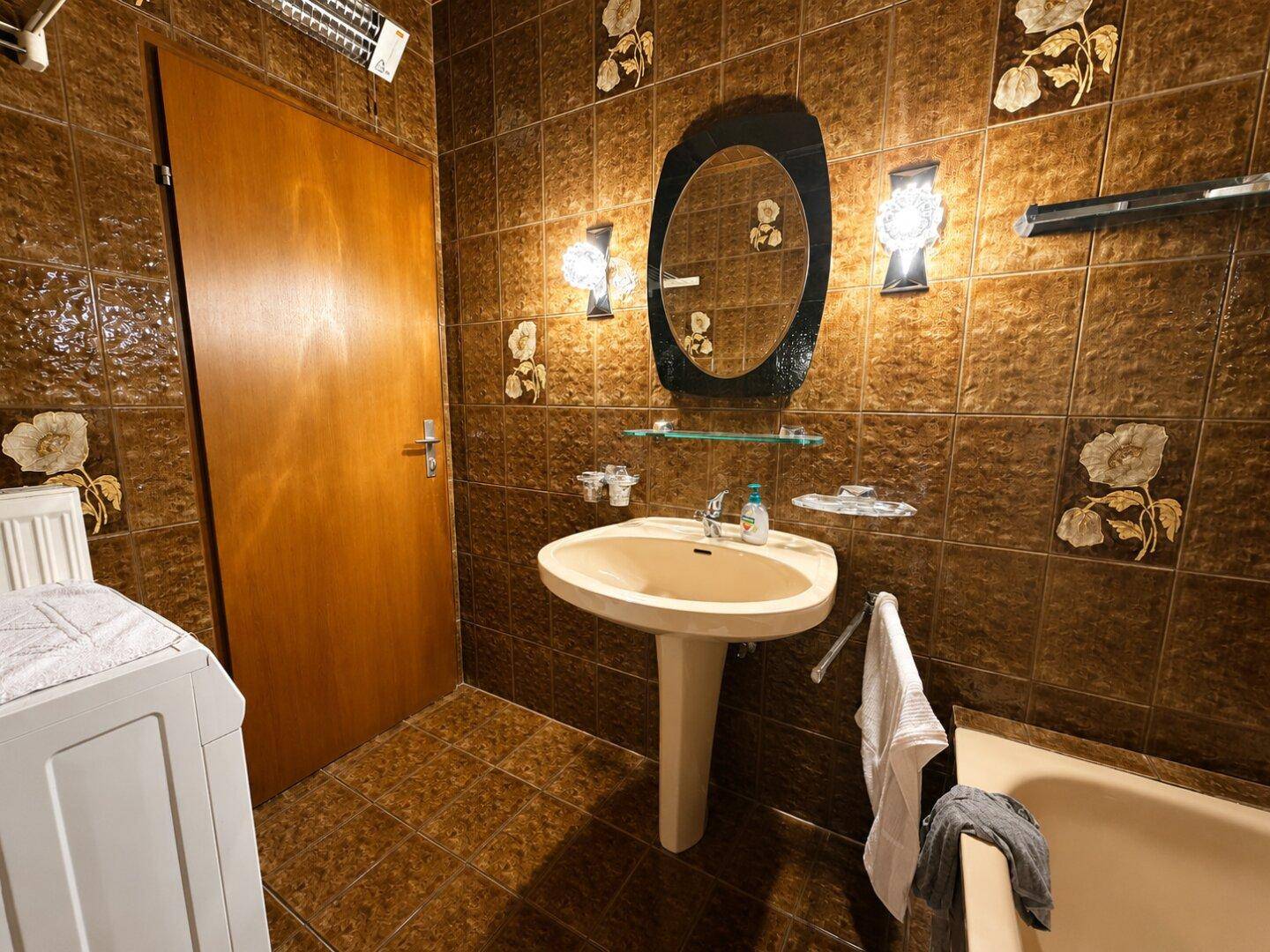 Badezimmer mit braunen Fliesen, Waschbecken und Spiegel über der Badewanne.