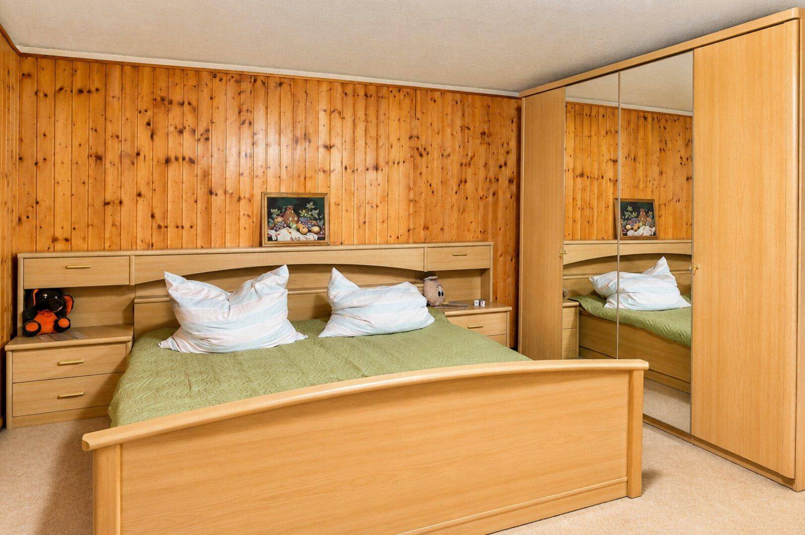 Schlafzimmer mit Holzvertäfelung, Doppelbett und Spiegelschrank.