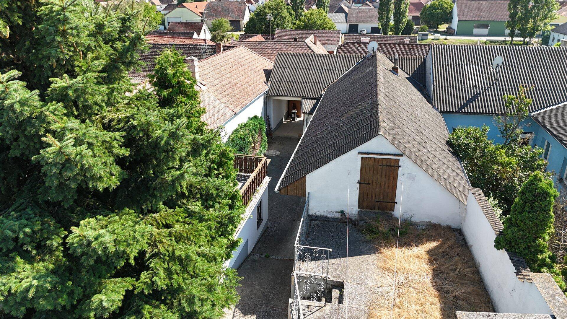 Vogelperspektive auf ein Grundstück mit Gebäuden, Bäumen und einem gepflasterten Bereich.
